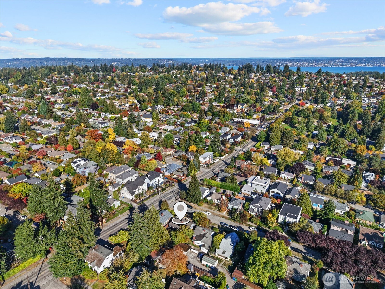 Aerial neighborhood view with the marked home, autumn trees, and water in the distance.