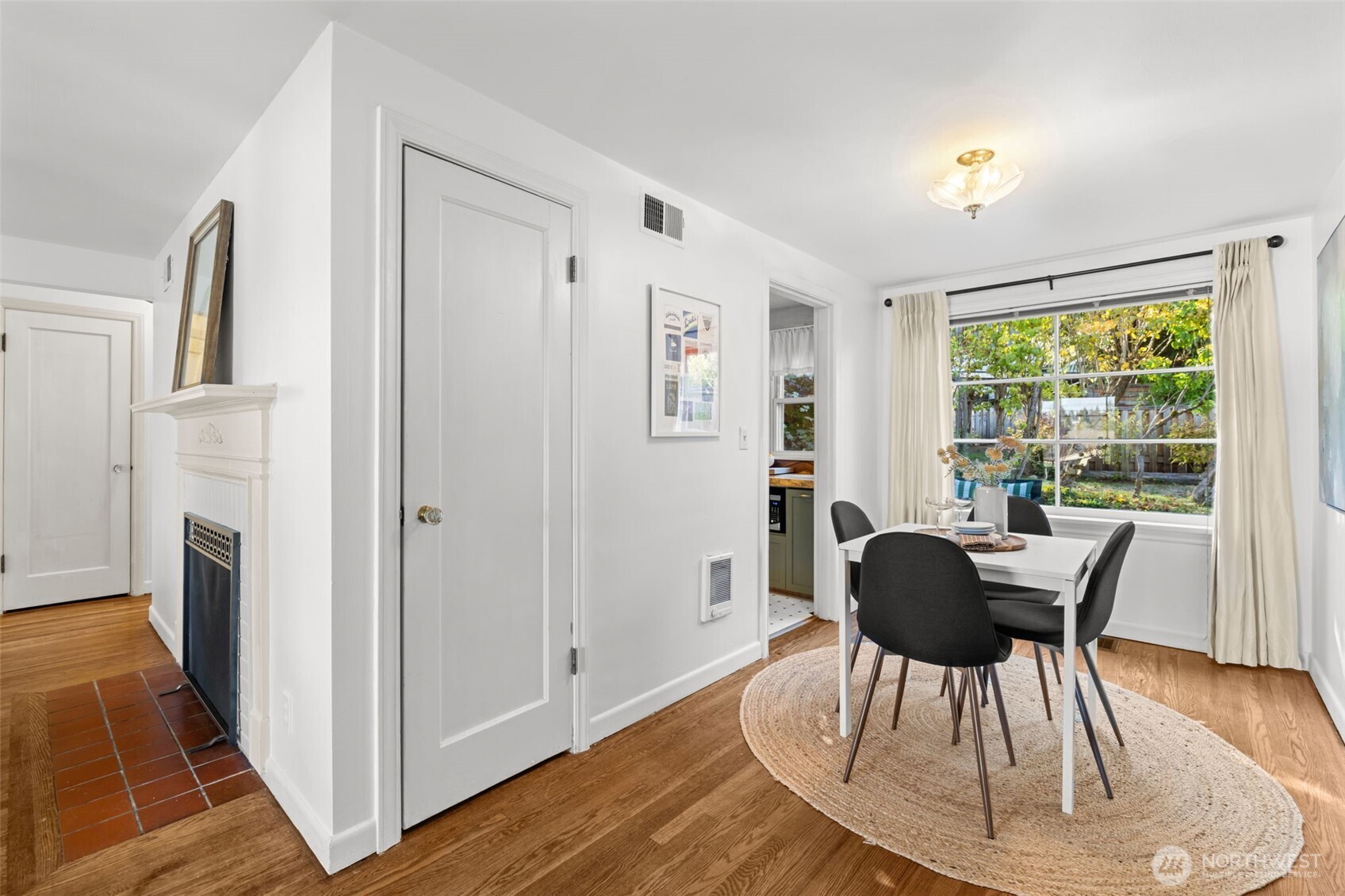 Dining area with a white table, dark chairs, hardwood floors, and a large window overlooking the backyard.