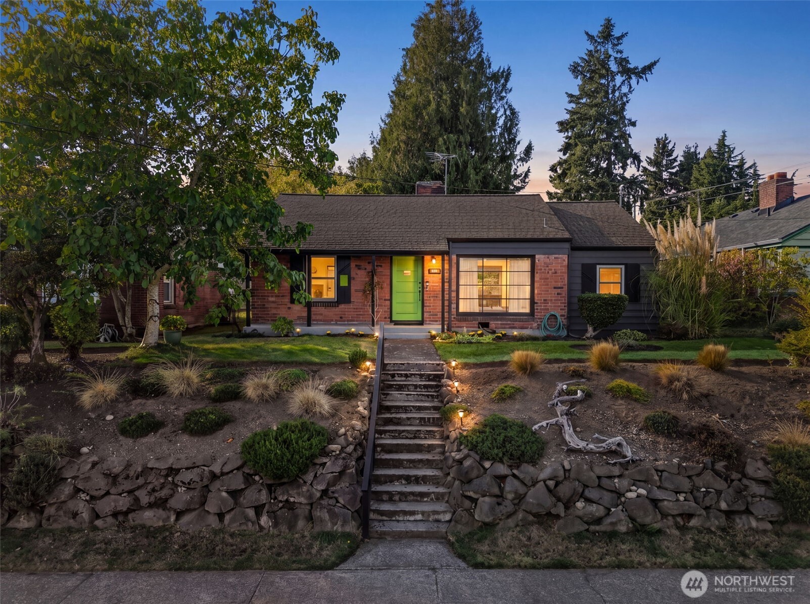 Brick house with a bright green front door, broad stone steps, and terraced landscaping at dusk.
