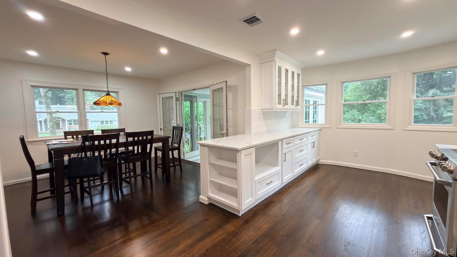 Open kitchen and dining area with a long white island, dark wood floors, and a stained-glass pendant light.