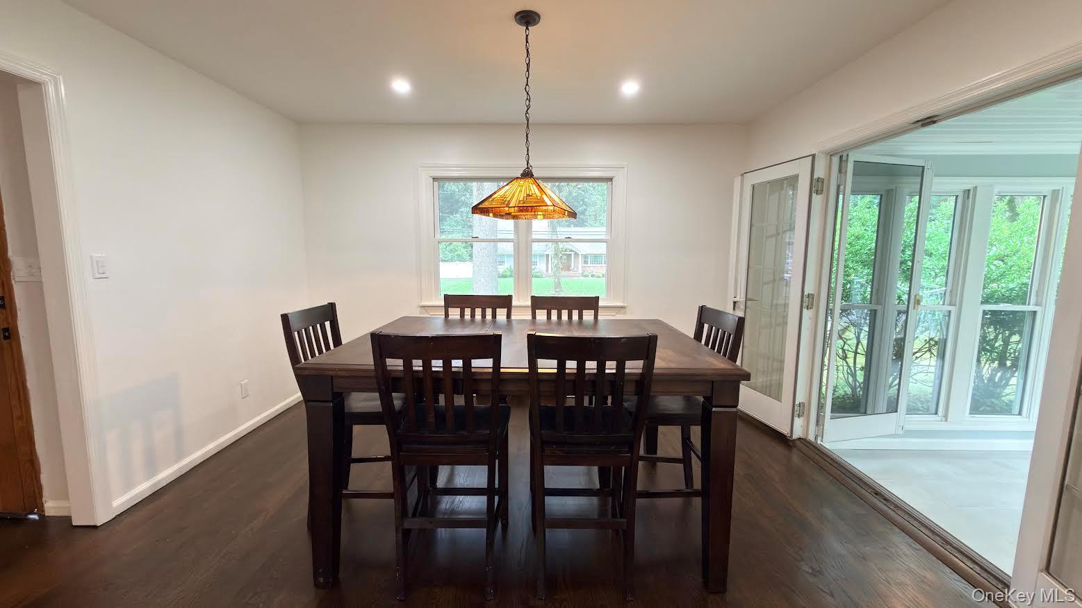 Dining room with a dark wood table, hardwood floors, and an open doorway to a sunroom.