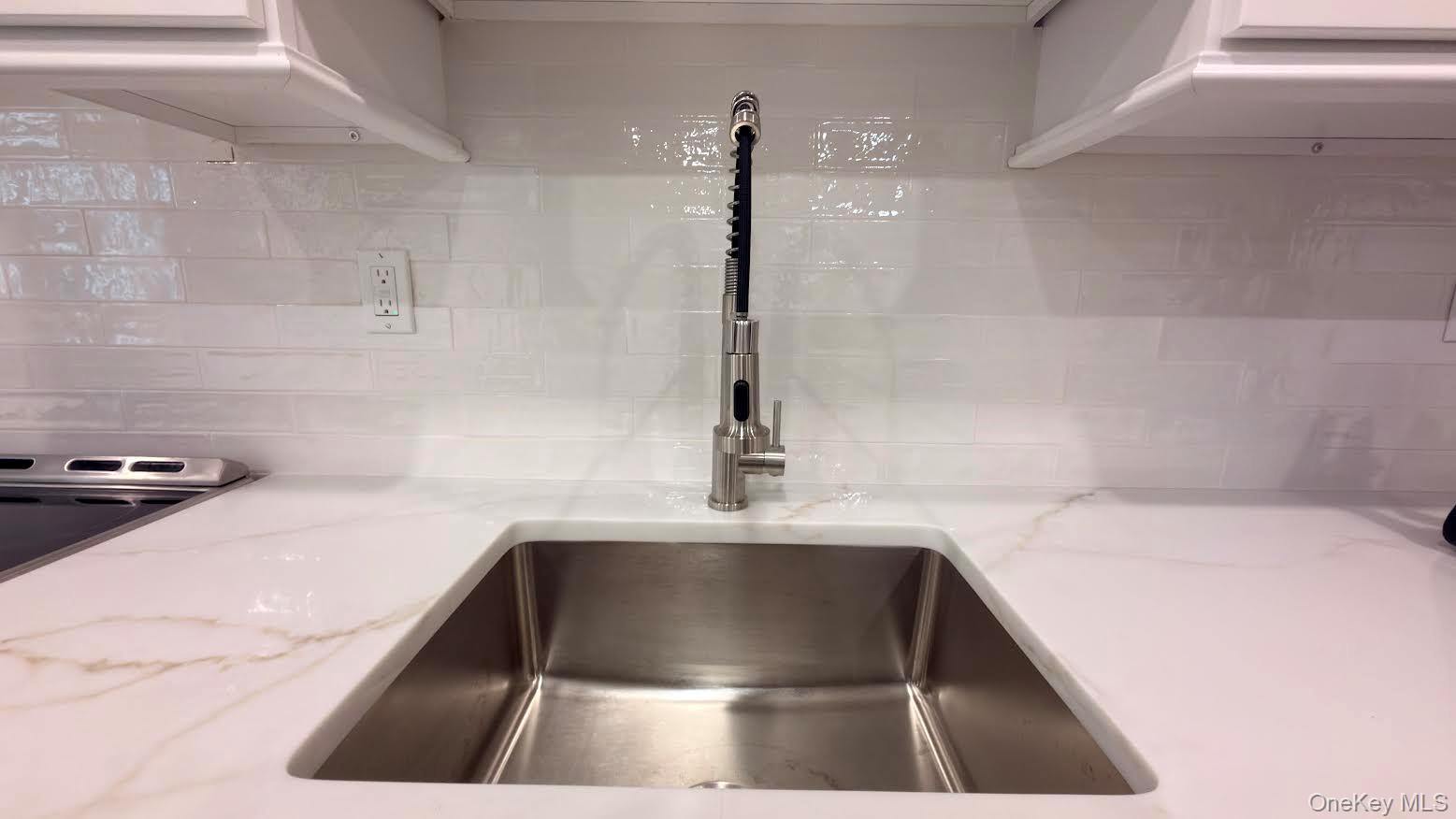 Kitchen sink with a tall pull-down faucet, white veined counters, and glossy tile backsplash.