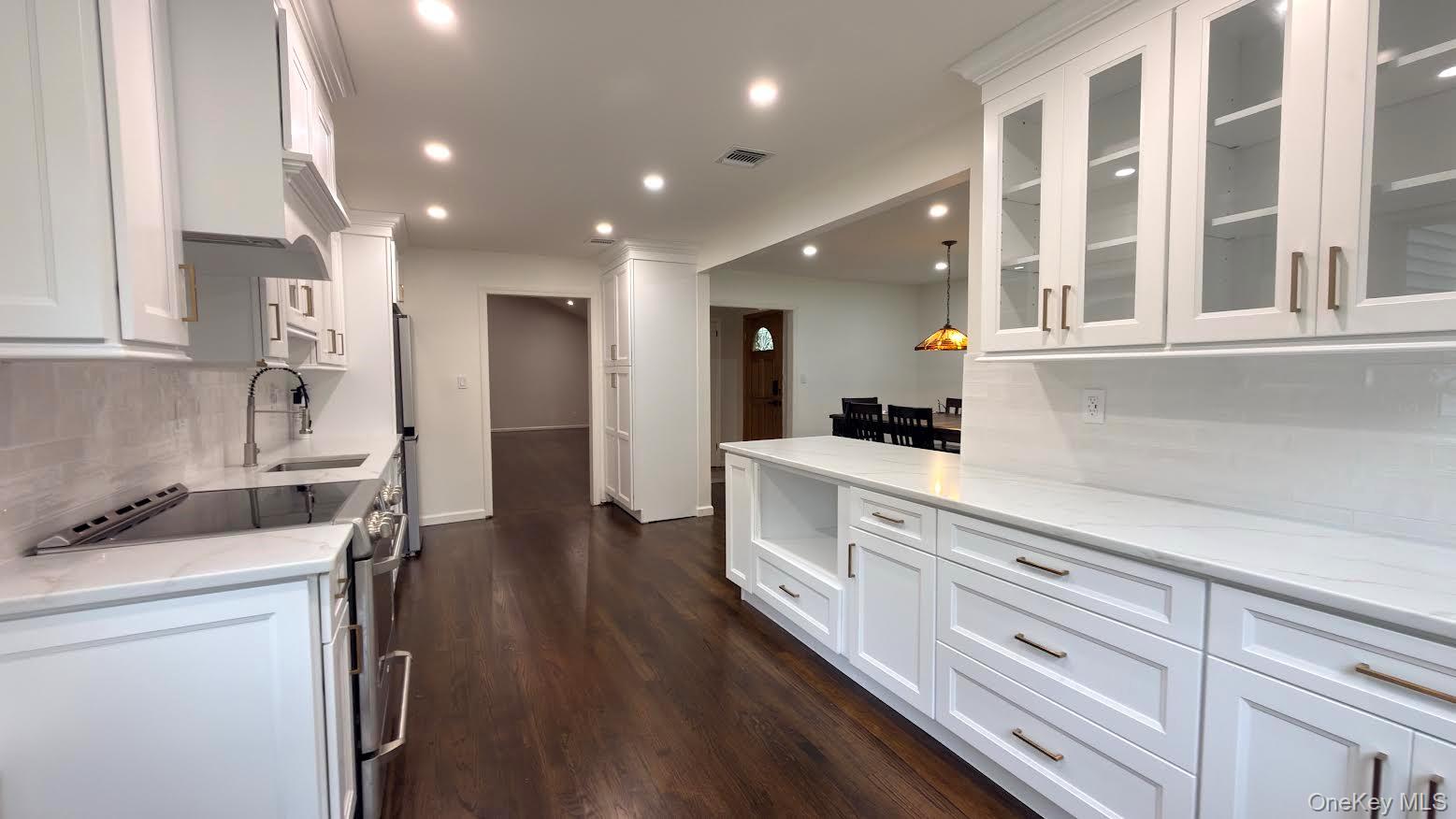 Renovated white kitchen with glass-front cabinets, stainless appliances, and dark hardwood floors.