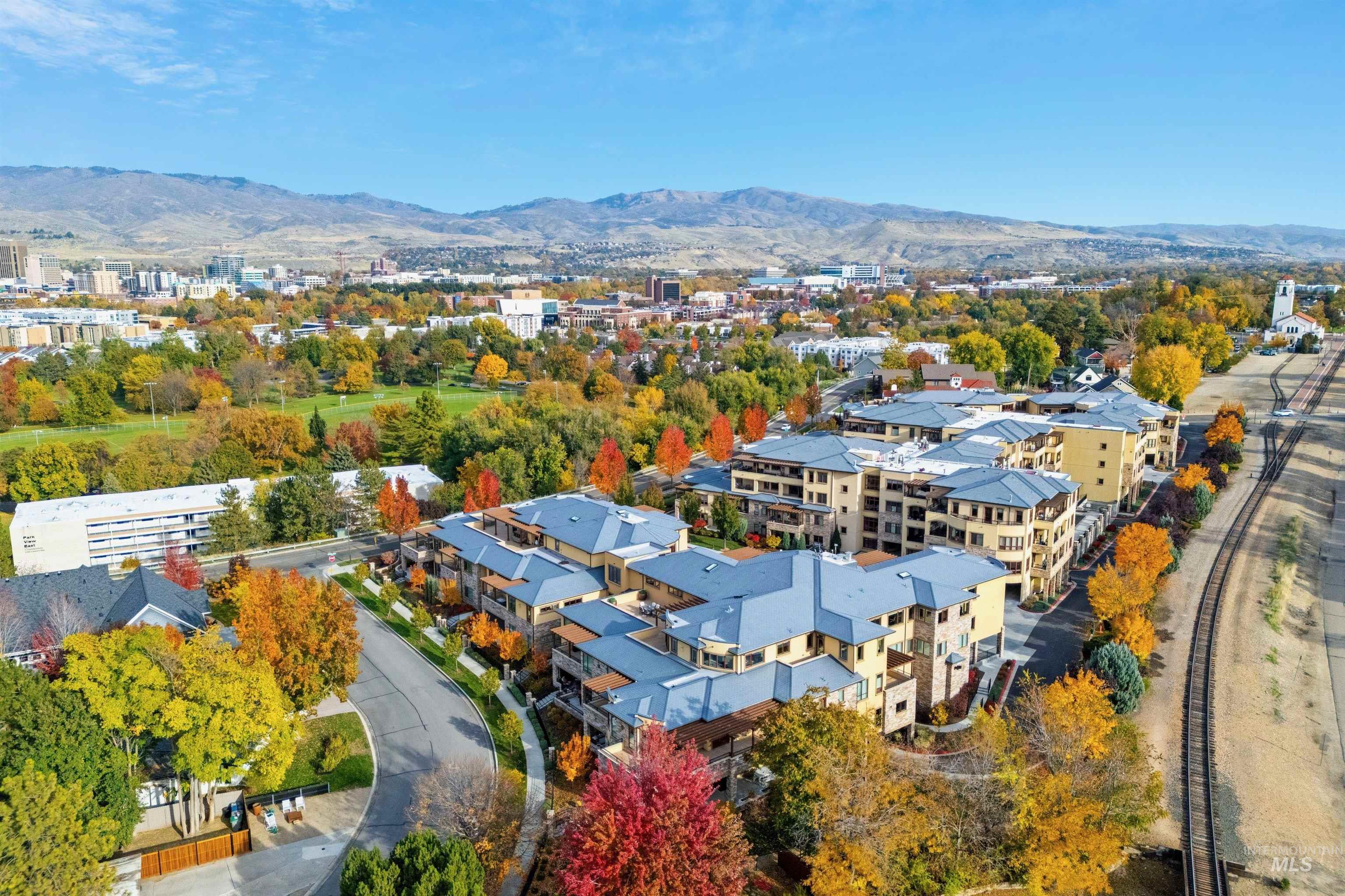 Aerial neighborhood of multifamily buildings and autumn trees beneath the foothills.