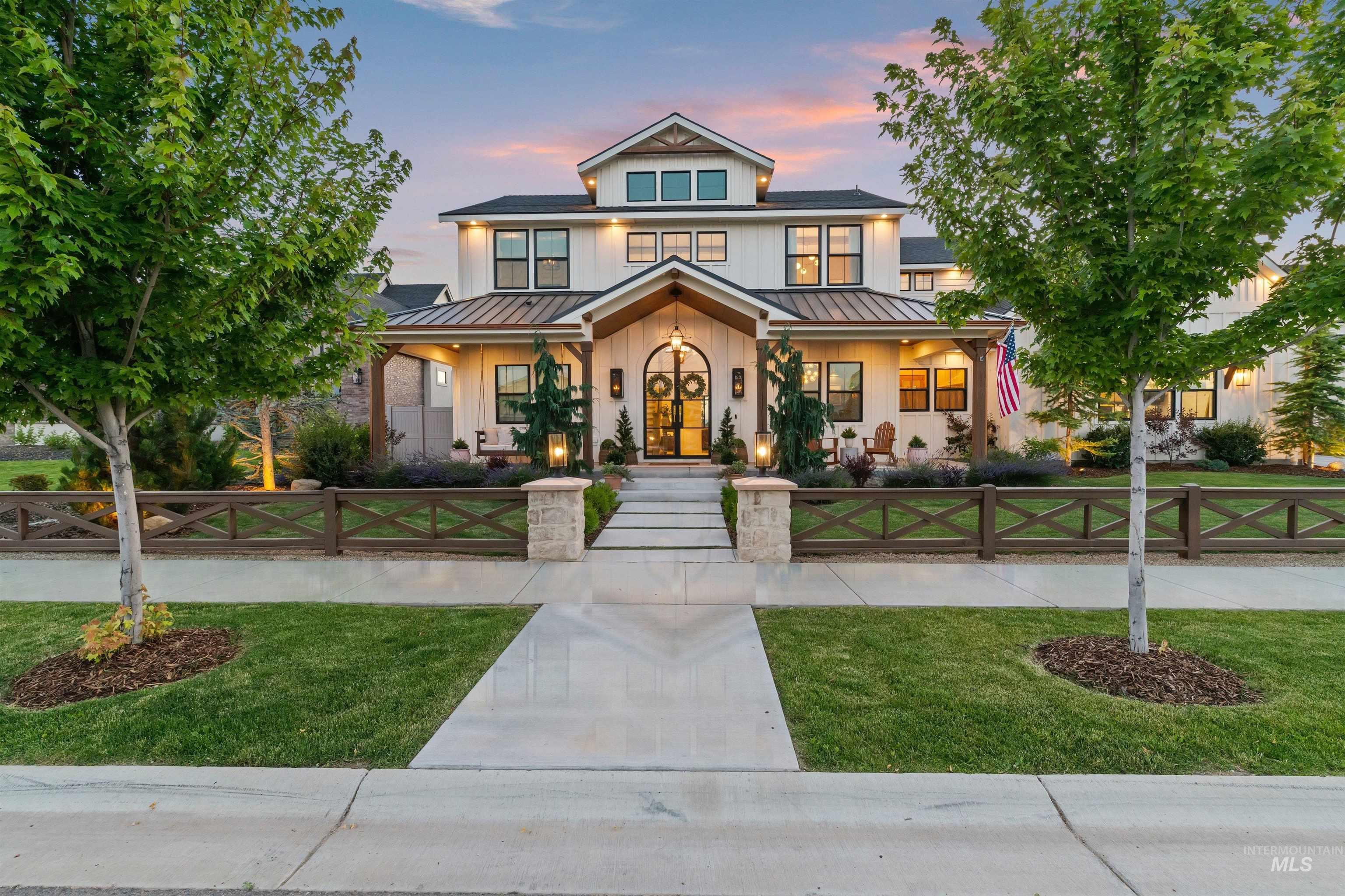 White two-story home with a covered porch, landscaped lawn, and wooden fence at dusk.
