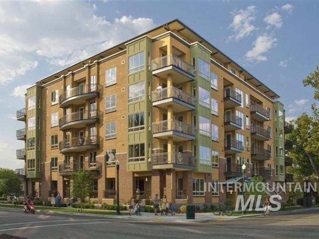 Multi-story apartment building with balconies on a sunny street corner.