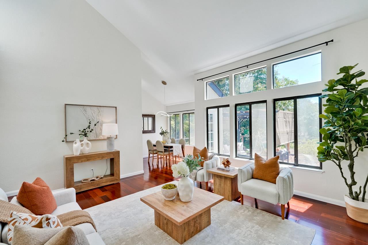 Staged living room with vaulted ceiling, expansive windows, and hardwood floors.