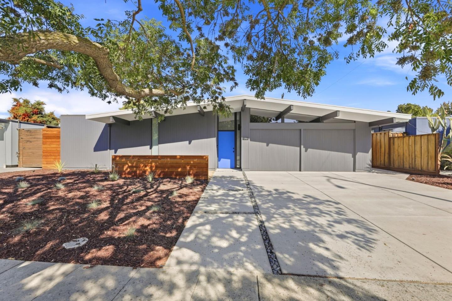 Modern gray home with a bright blue front door, broad roof, and wide concrete driveway.