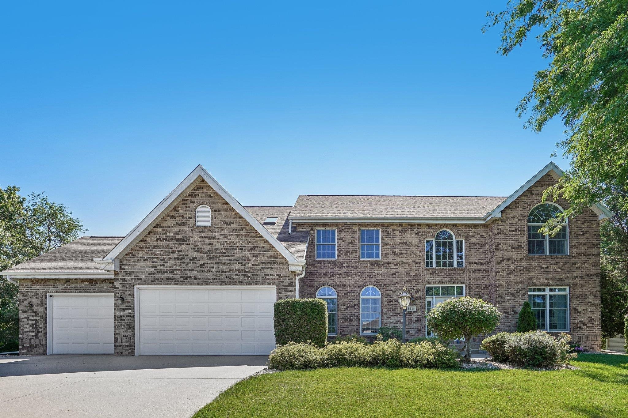 Two-story brick house with multiple gables, two garage doors, and landscaped front yard.