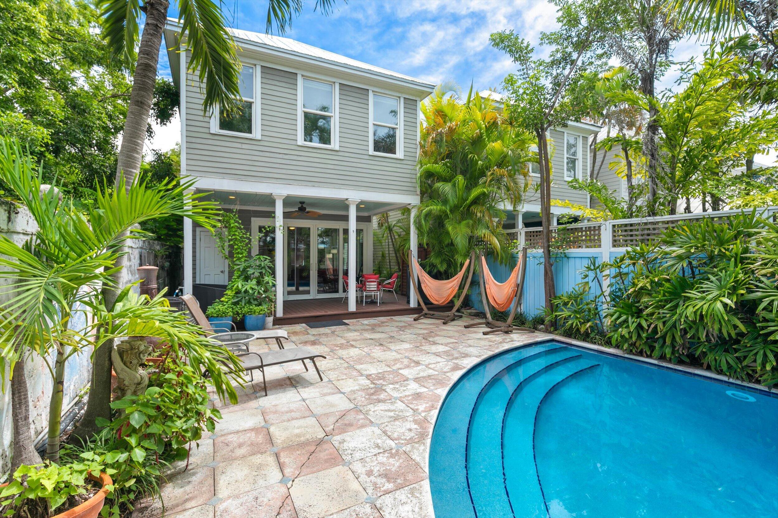 Home’s tropical backyard with a curved pool, stone patio, and two orange hammocks.