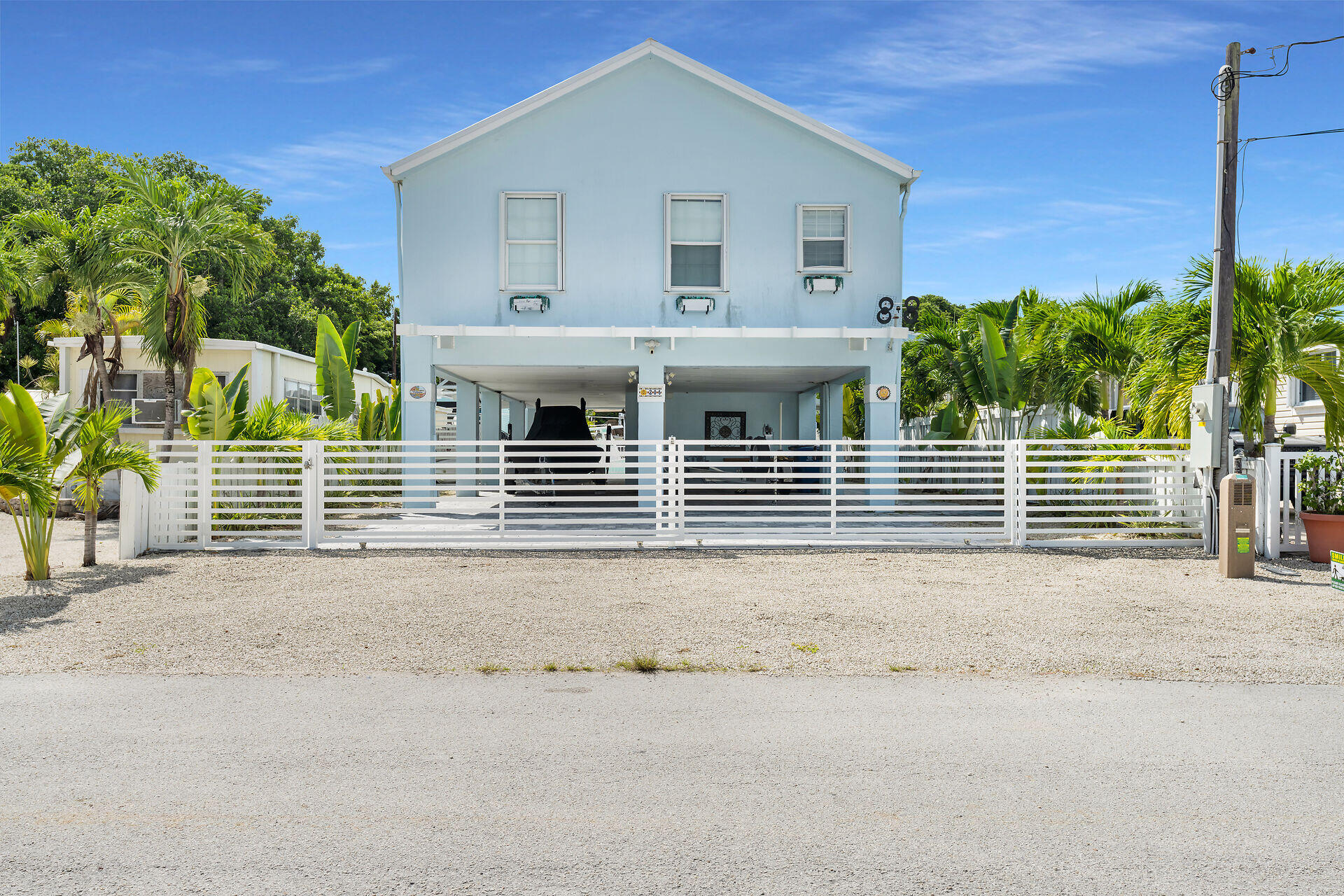 Pale blue elevated home behind a white gate, framed by tropical palms.