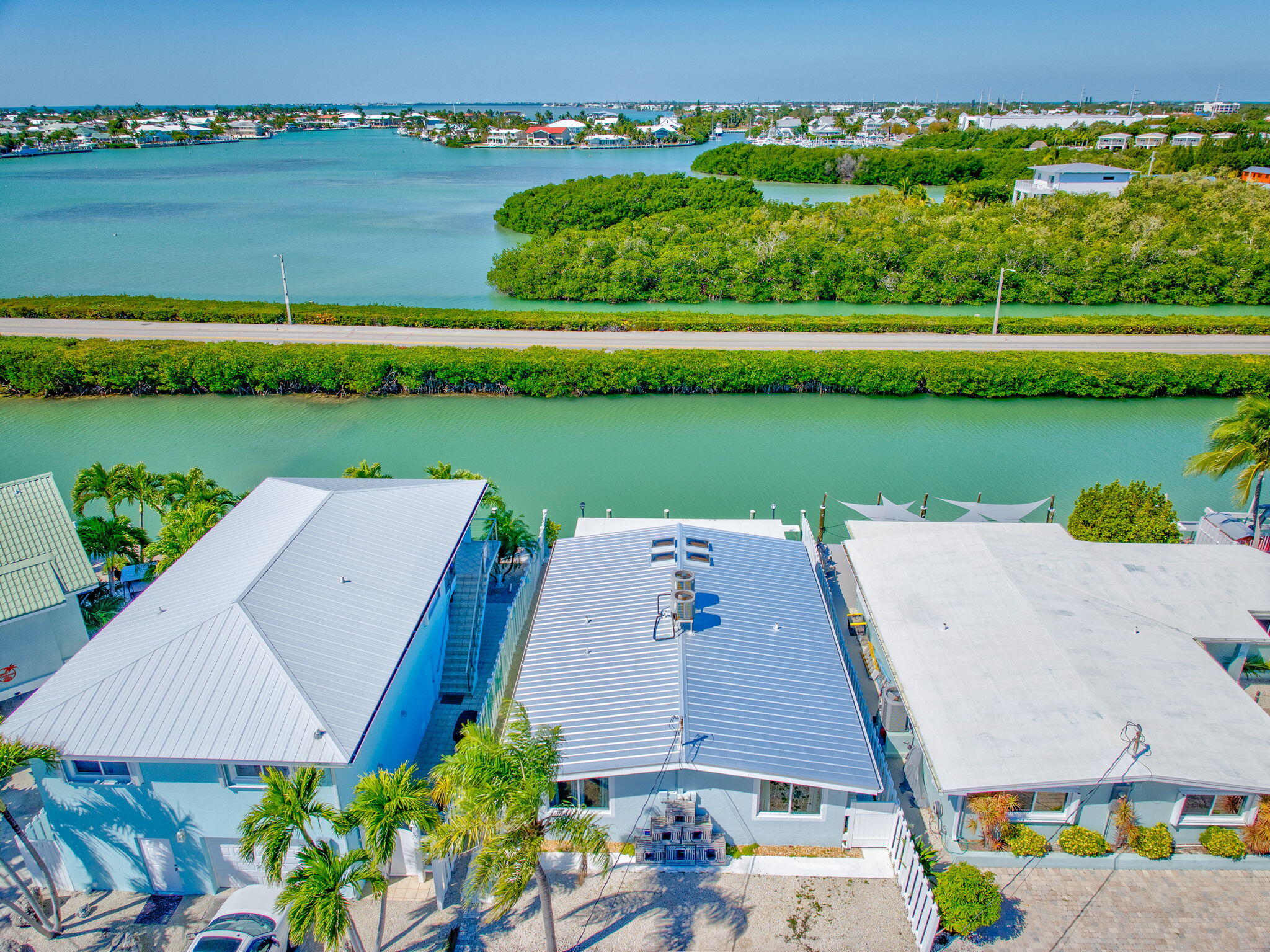 Aerial view of waterfront homes along a turquoise canal, with mangroves and homes across the water.