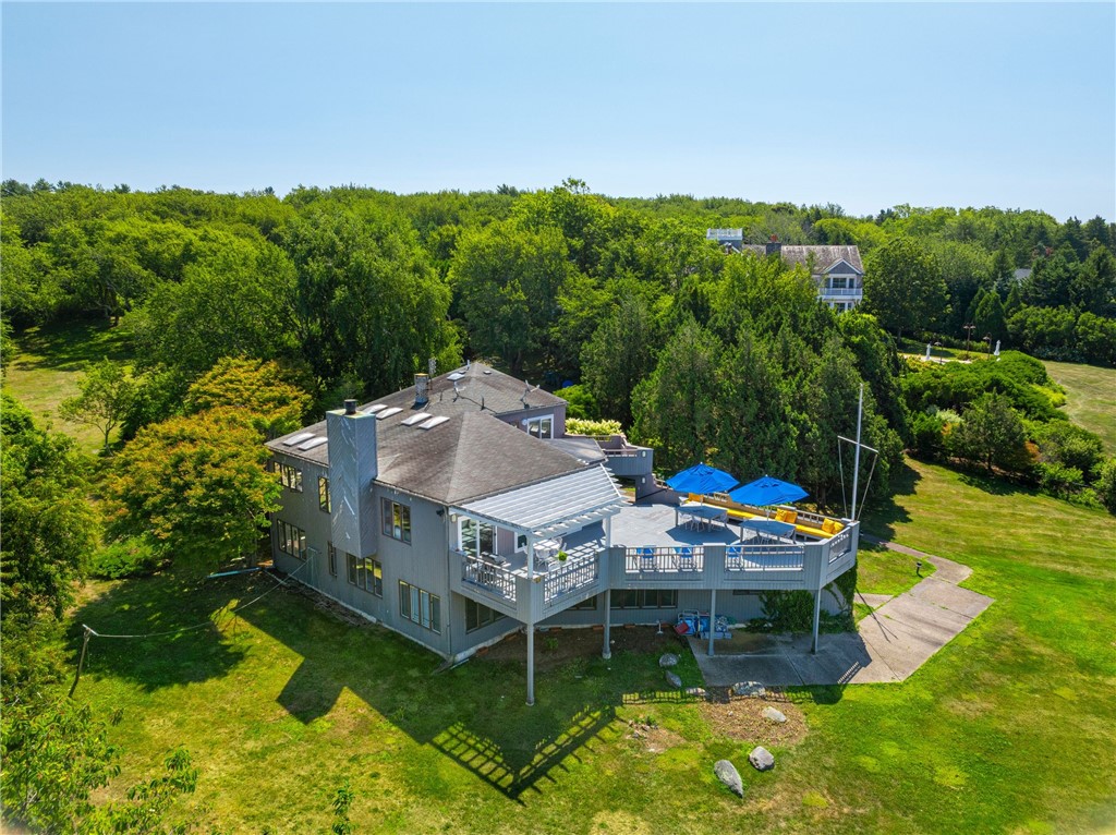 Gray-sided home with a raised deck, blue umbrellas, lawn, and mature trees.