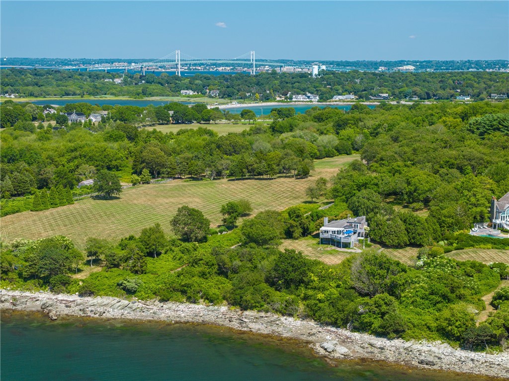Coastal home beside wooded grounds and rocky shoreline, with a suspension bridge in the distance.