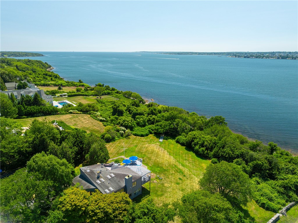 Waterfront home surrounded by trees and lawn, with a broad bay and distant shorelines beyond.