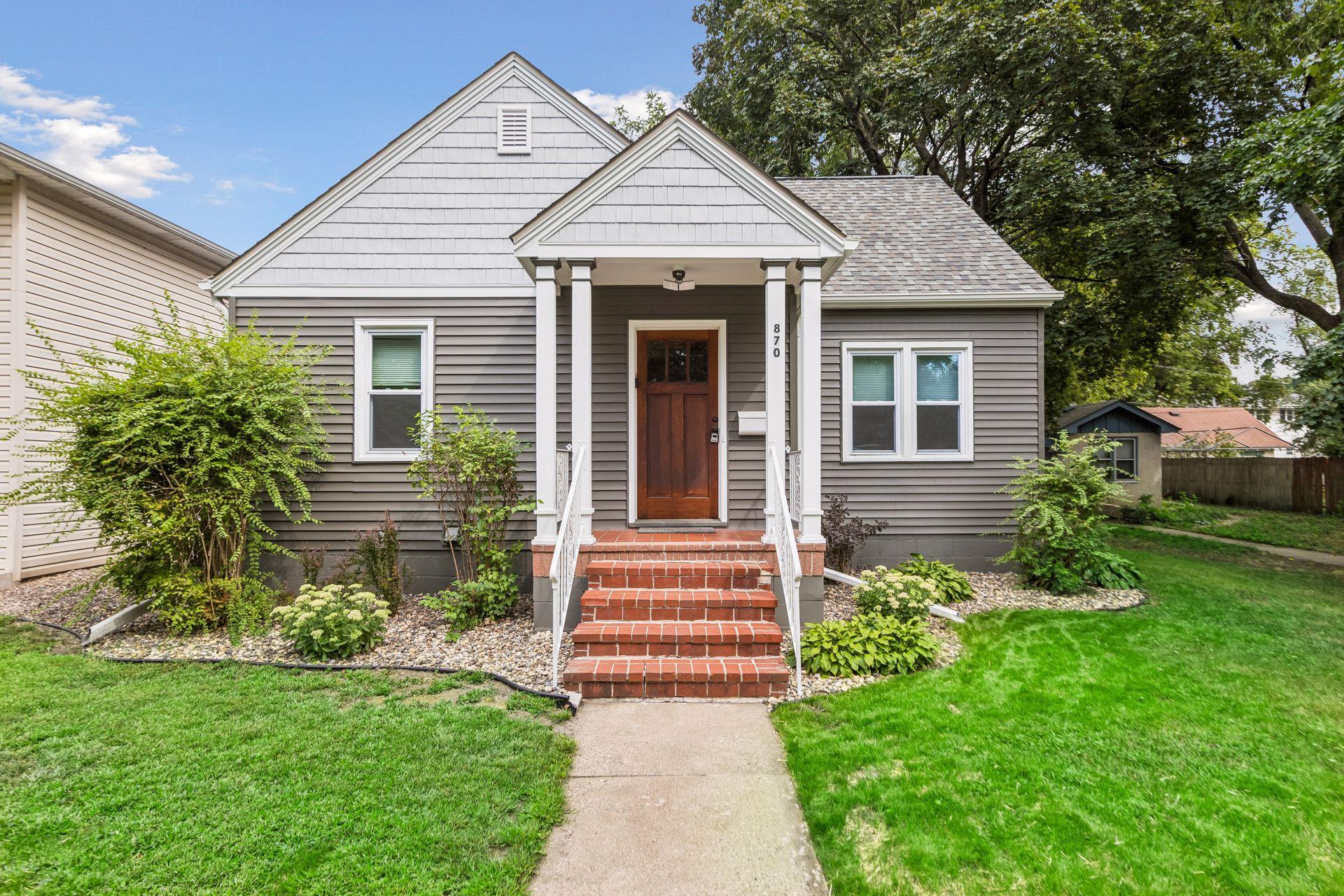 Gray-sided house with white trim, a wooden front door, and red brick steps.