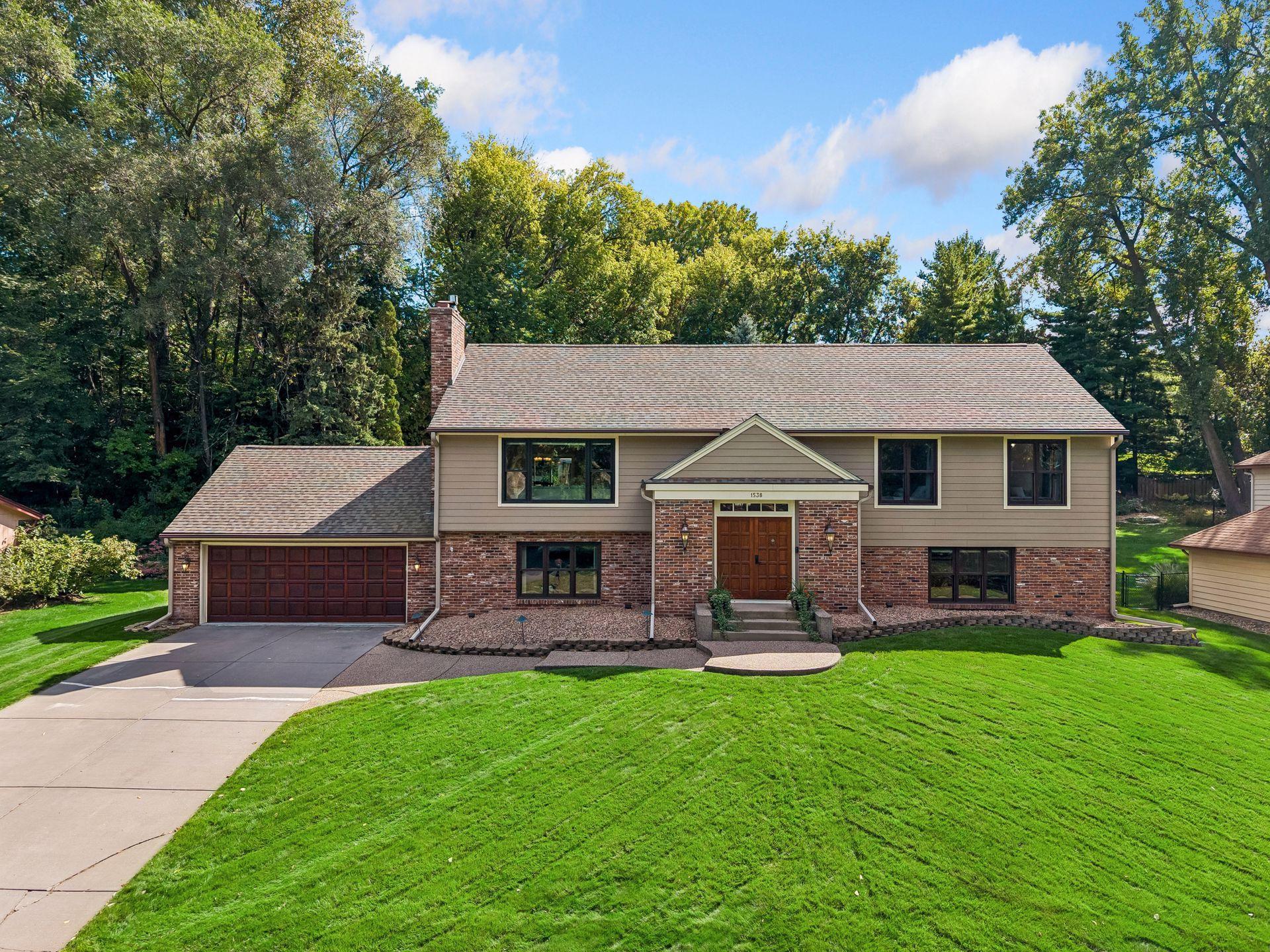 Two-story brick-and-siding home with a double garage, broad lawn, and mature trees.