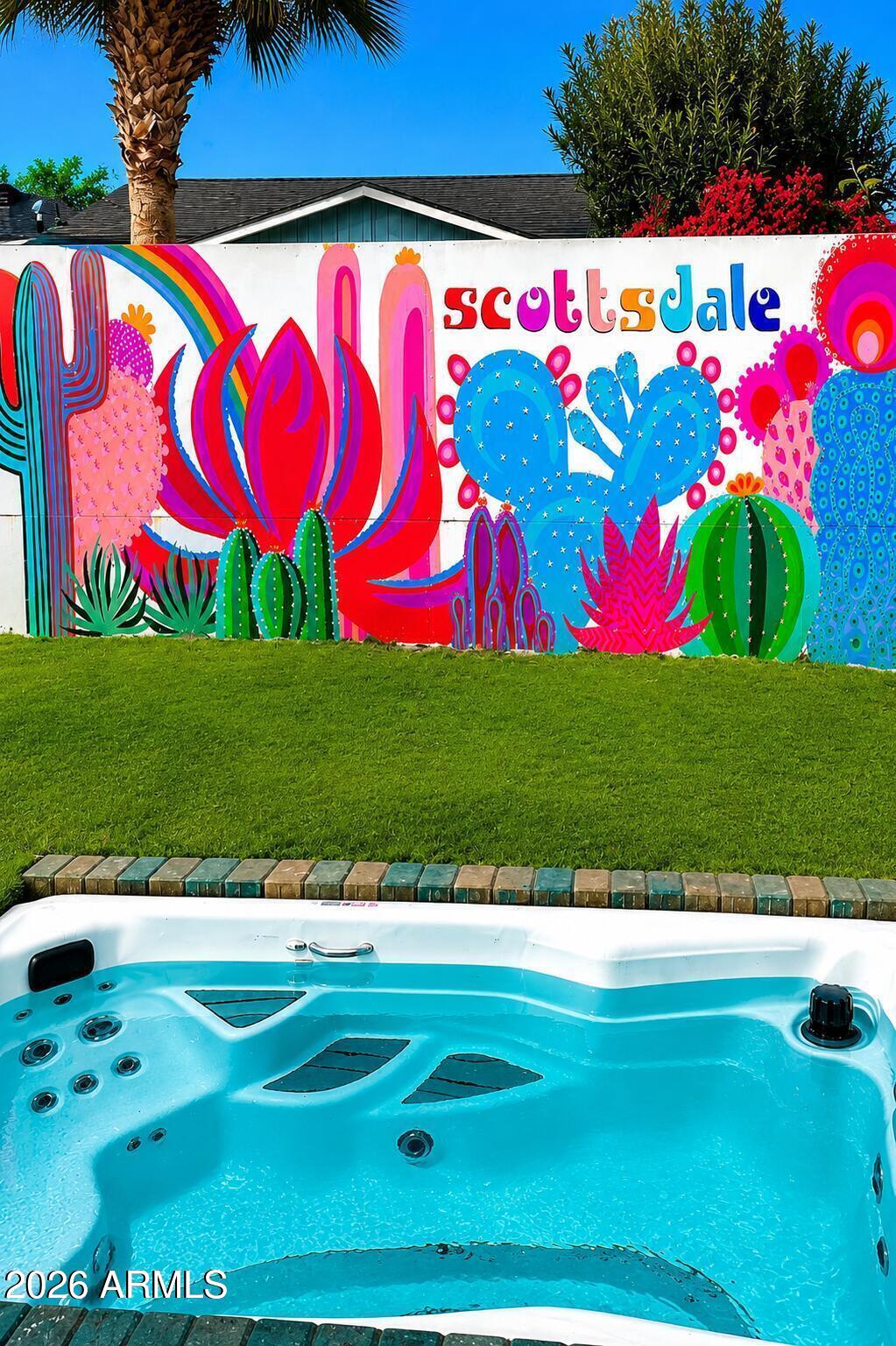 Outdoor hot tub beside a colorful Scottsdale cactus mural and lawn.