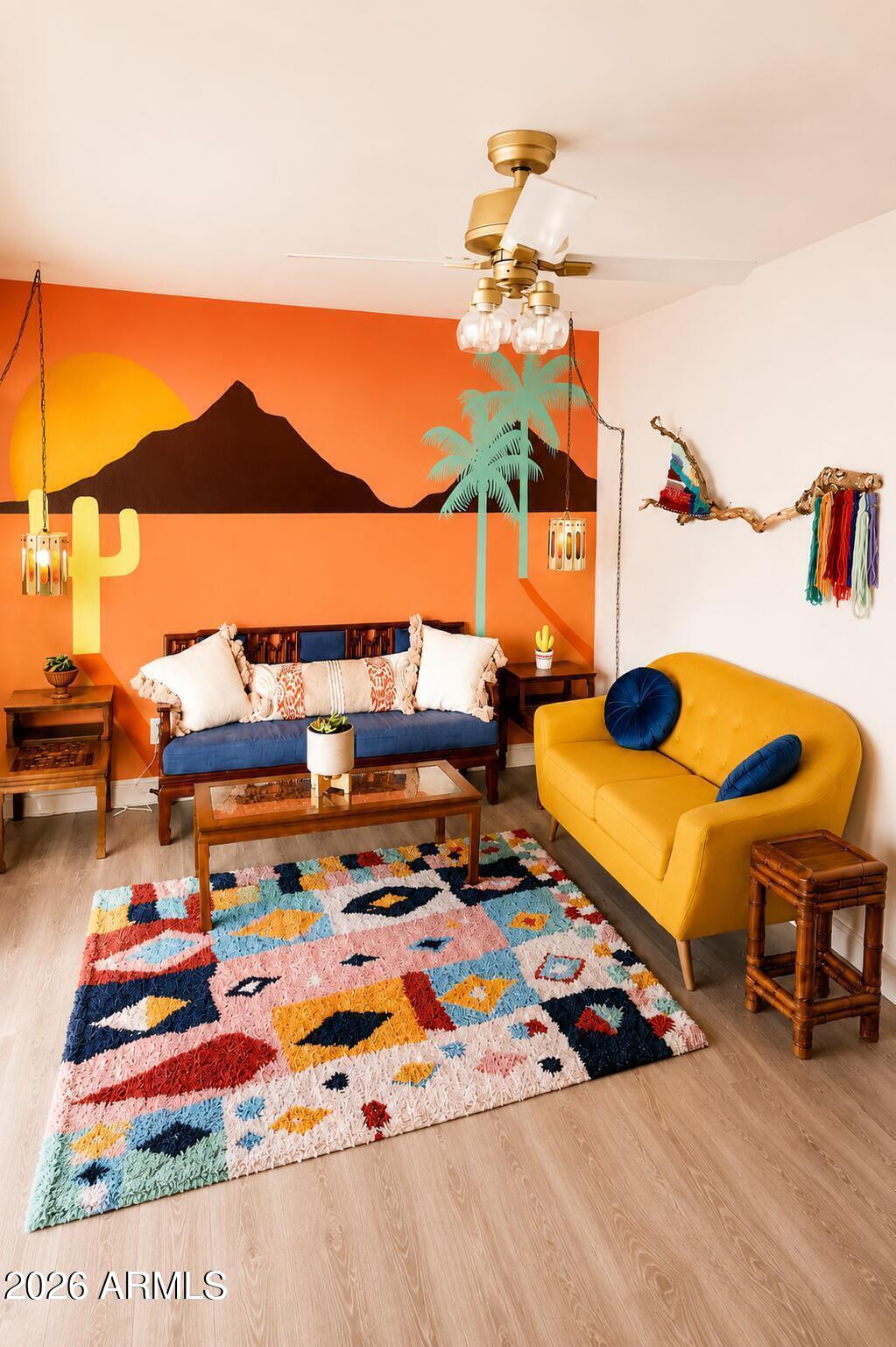 Colorful living room with a desert mural, blue daybed, mustard-yellow sofa, and patterned rug.