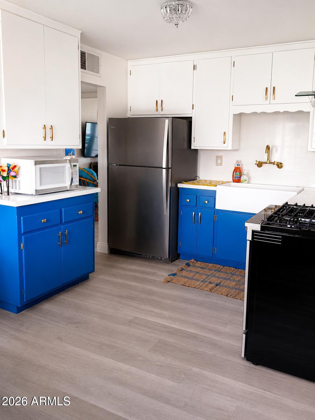 Kitchen with blue lower cabinets, white farmhouse sink, and stainless-steel refrigerator.