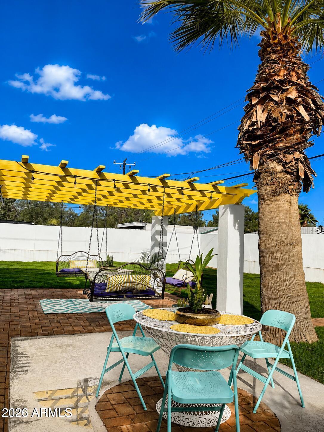 Patio with a yellow pergola, hanging swings, turquoise chairs, and a palm tree.