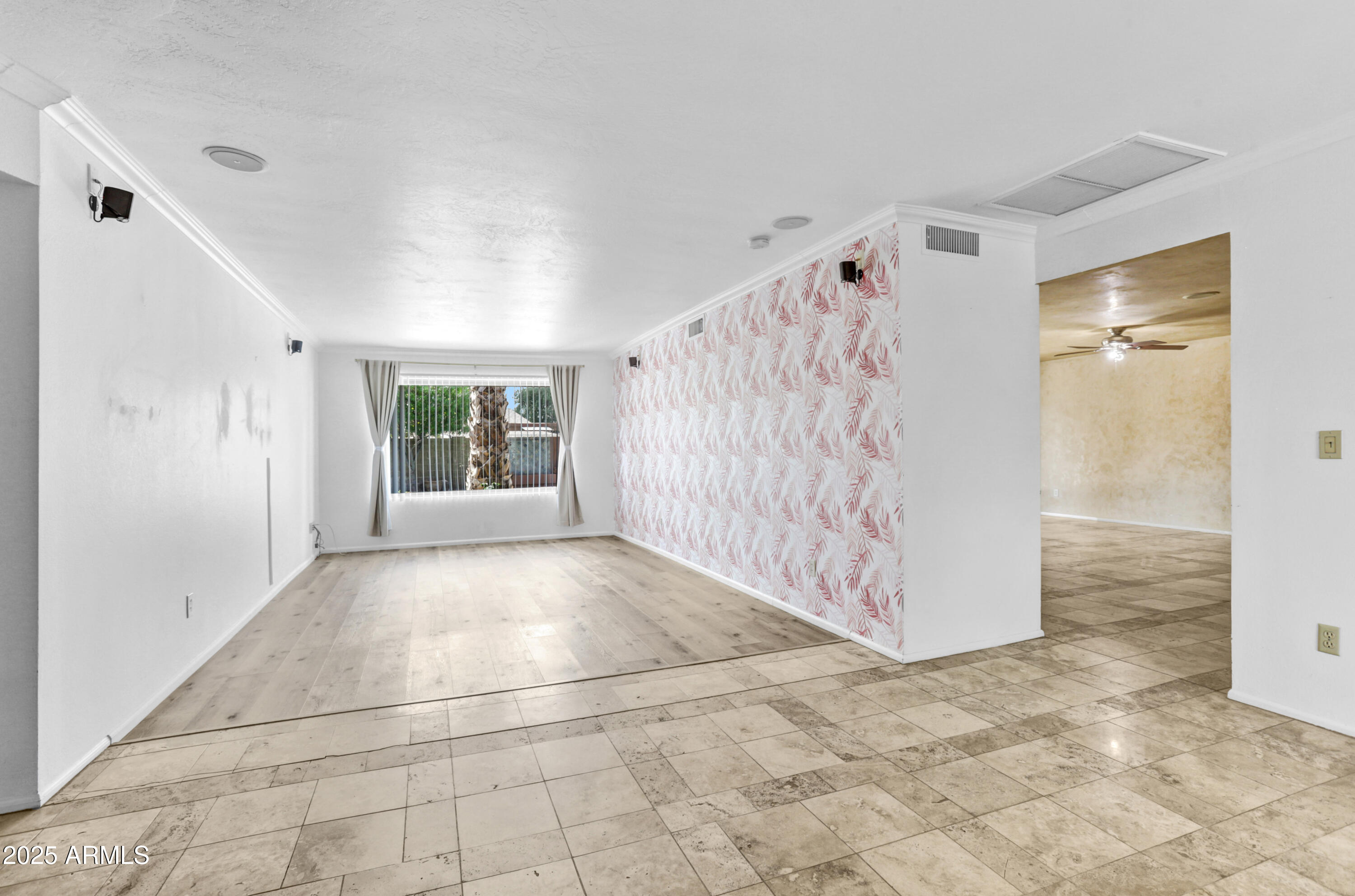 Empty living room with a patterned accent wall, wood-look flooring, and a window with vertical blinds.