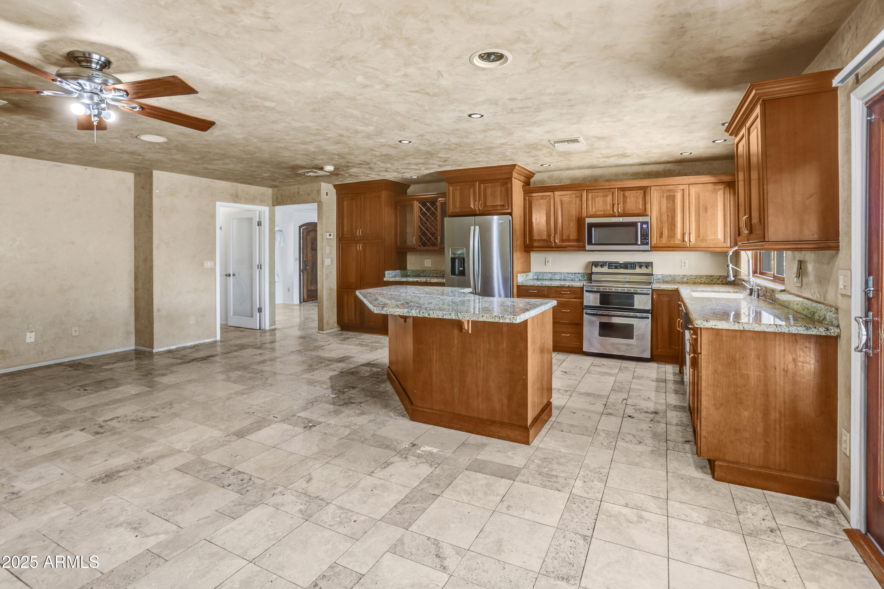 Kitchen with a granite-topped island, warm wood cabinetry, stainless steel appliances, and gray tile floors.