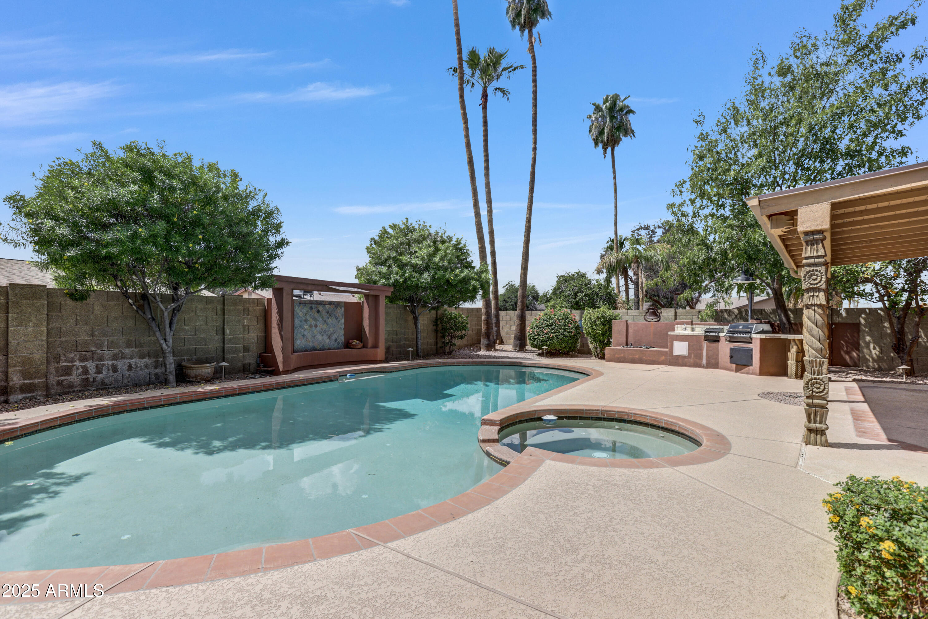 Backyard pool and circular spa beside an outdoor kitchen and tiled water feature.