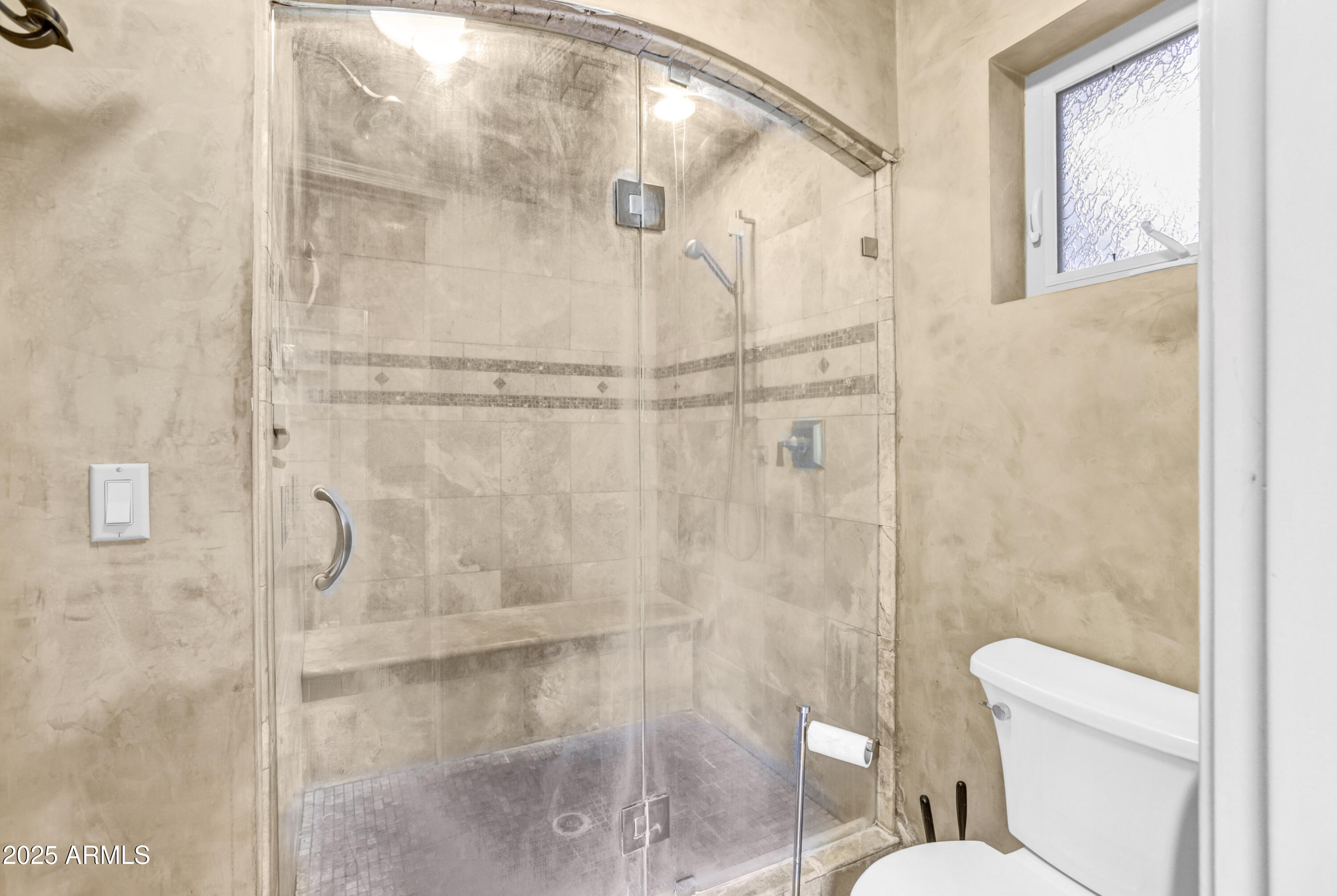Bathroom with a glass-enclosed tiled shower, built-in bench, and small window.
