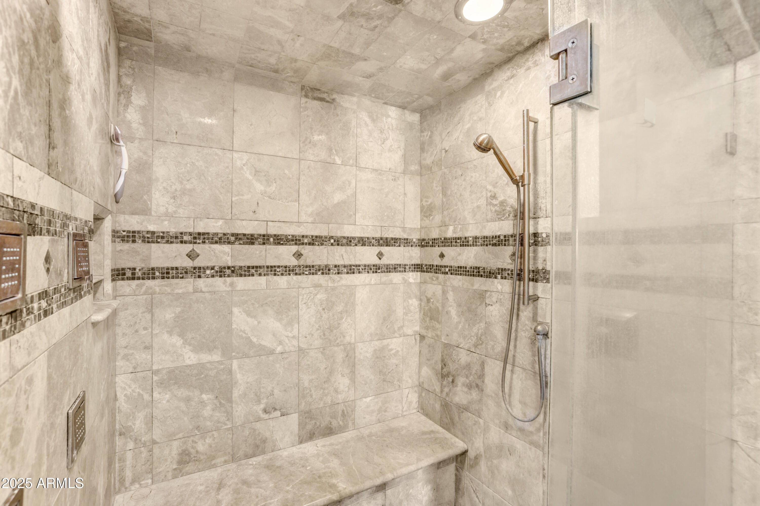 Walk-in shower with a built-in stone bench, glass enclosure, and decorative mosaic tile bands.