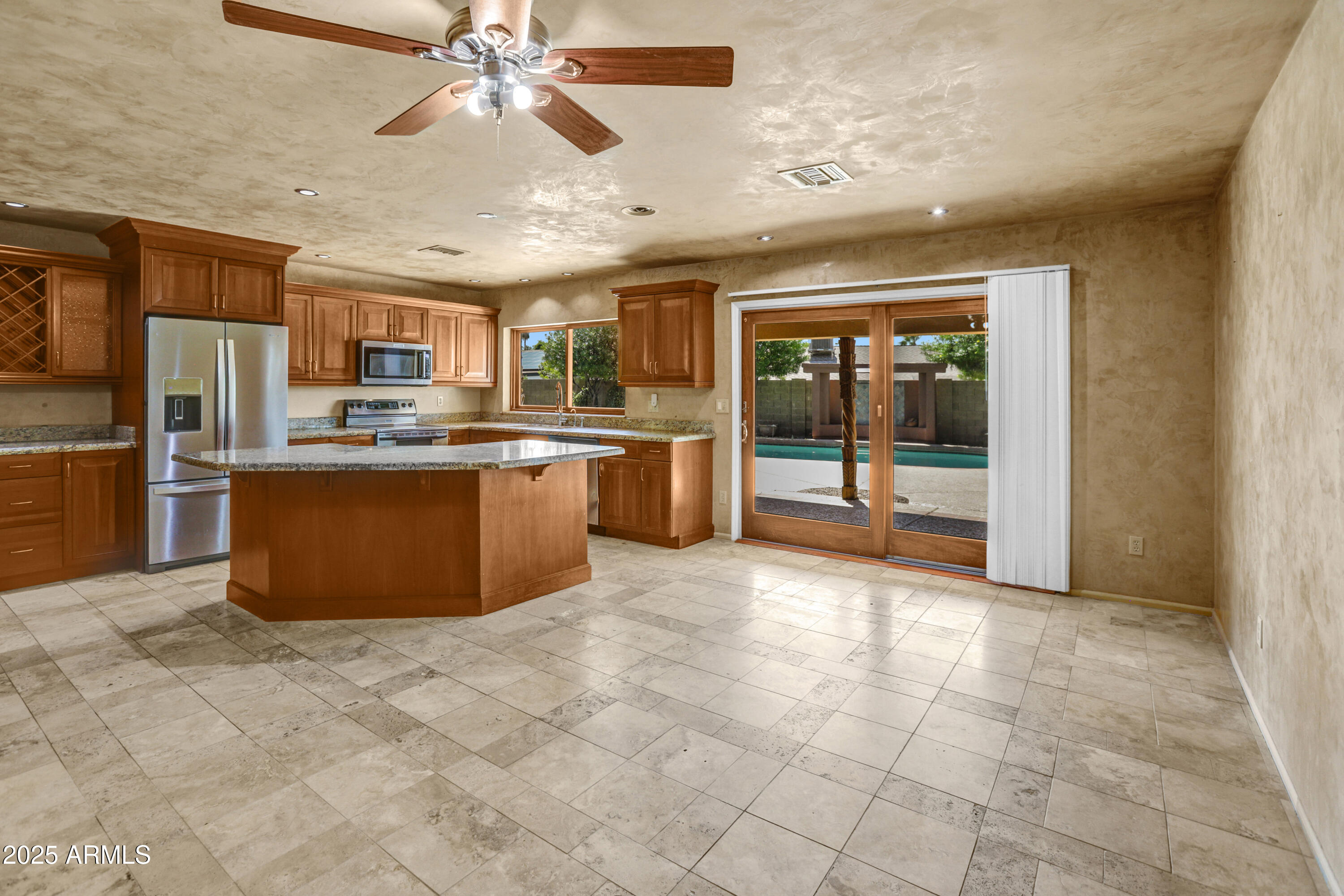 Kitchen with wood cabinetry, a granite island, stainless appliances, and sliding doors facing a pool.