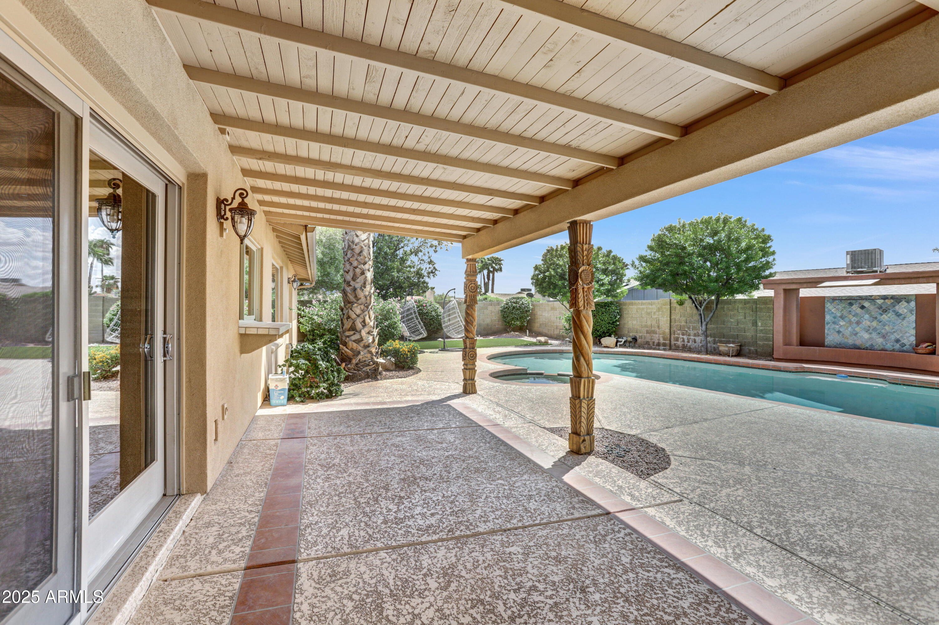 Covered patio beside a backyard pool, with carved columns and a tiled water feature.