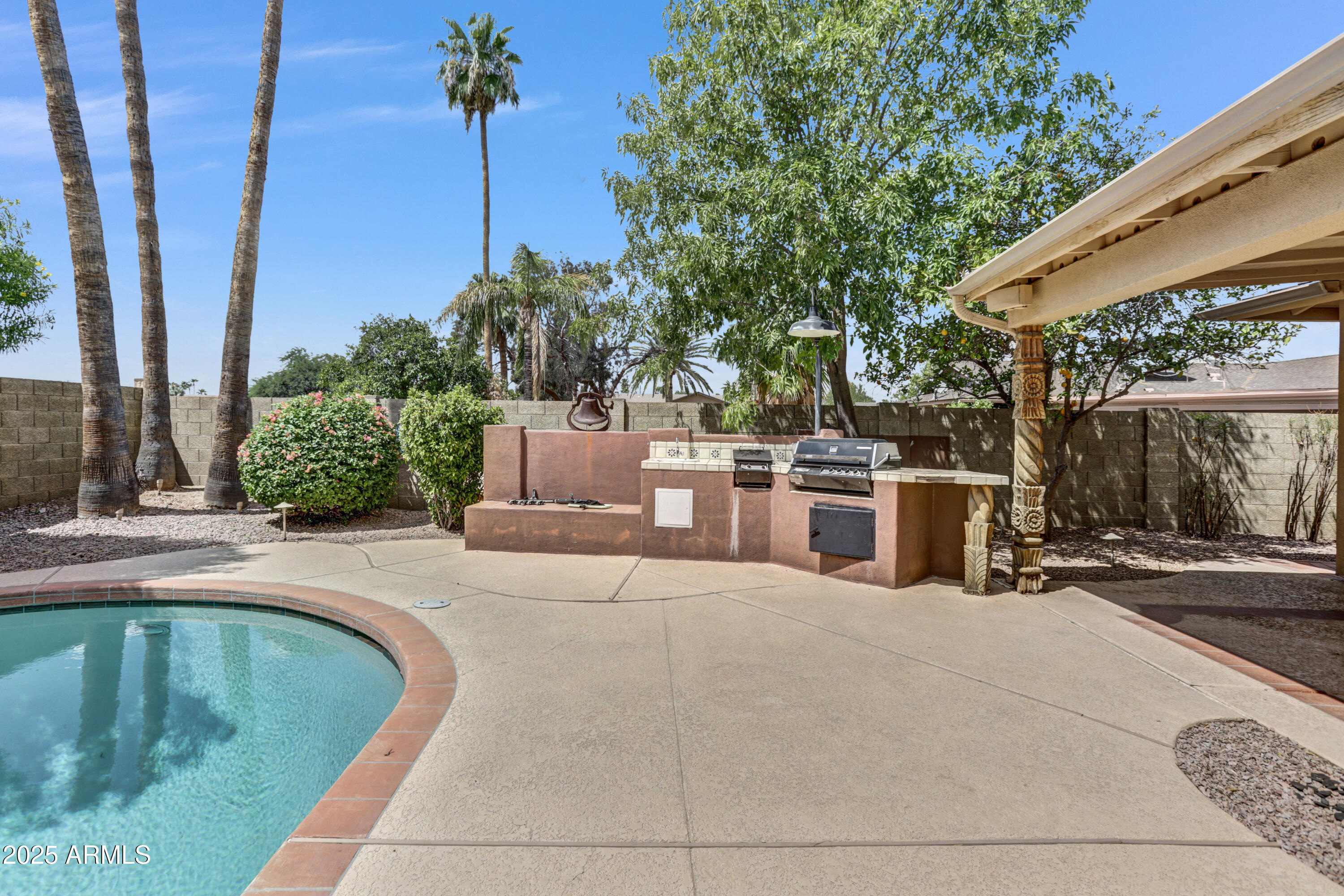 Backyard pool beside a built-in outdoor grill and covered pergola.