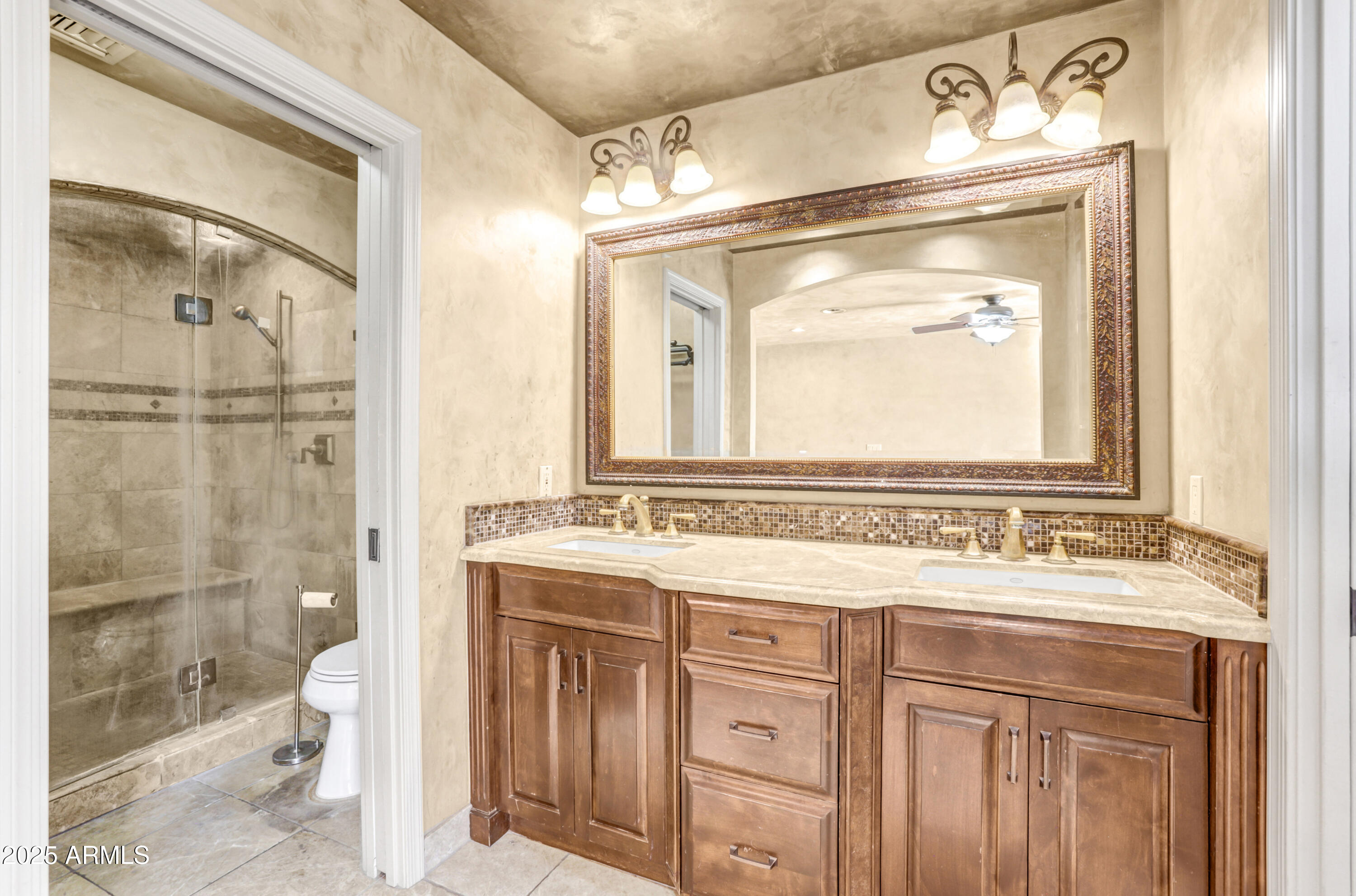 Bathroom with a double-sink wood vanity, ornate mirror, and glass-enclosed tiled shower.