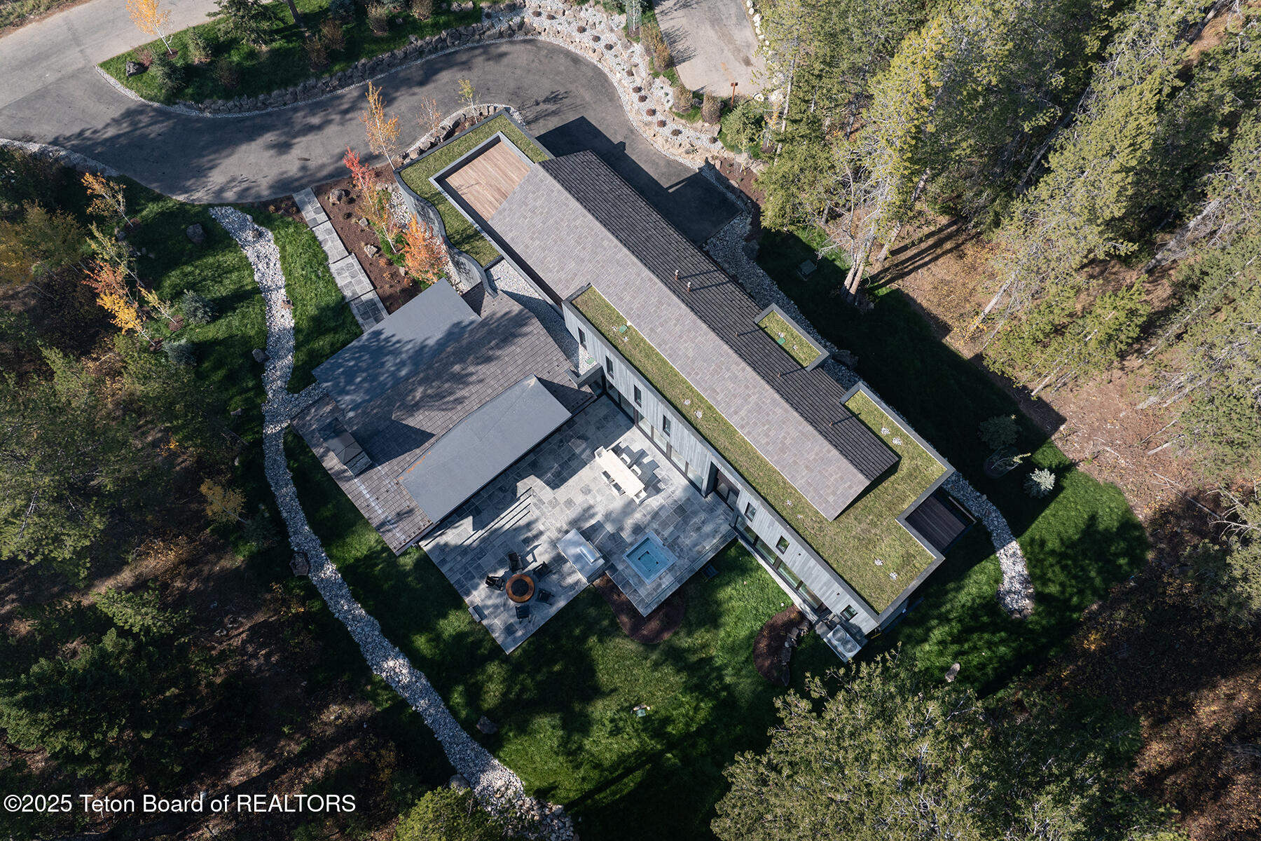 Modern home with green roof sections, stone patio, and landscaped grounds viewed from above.