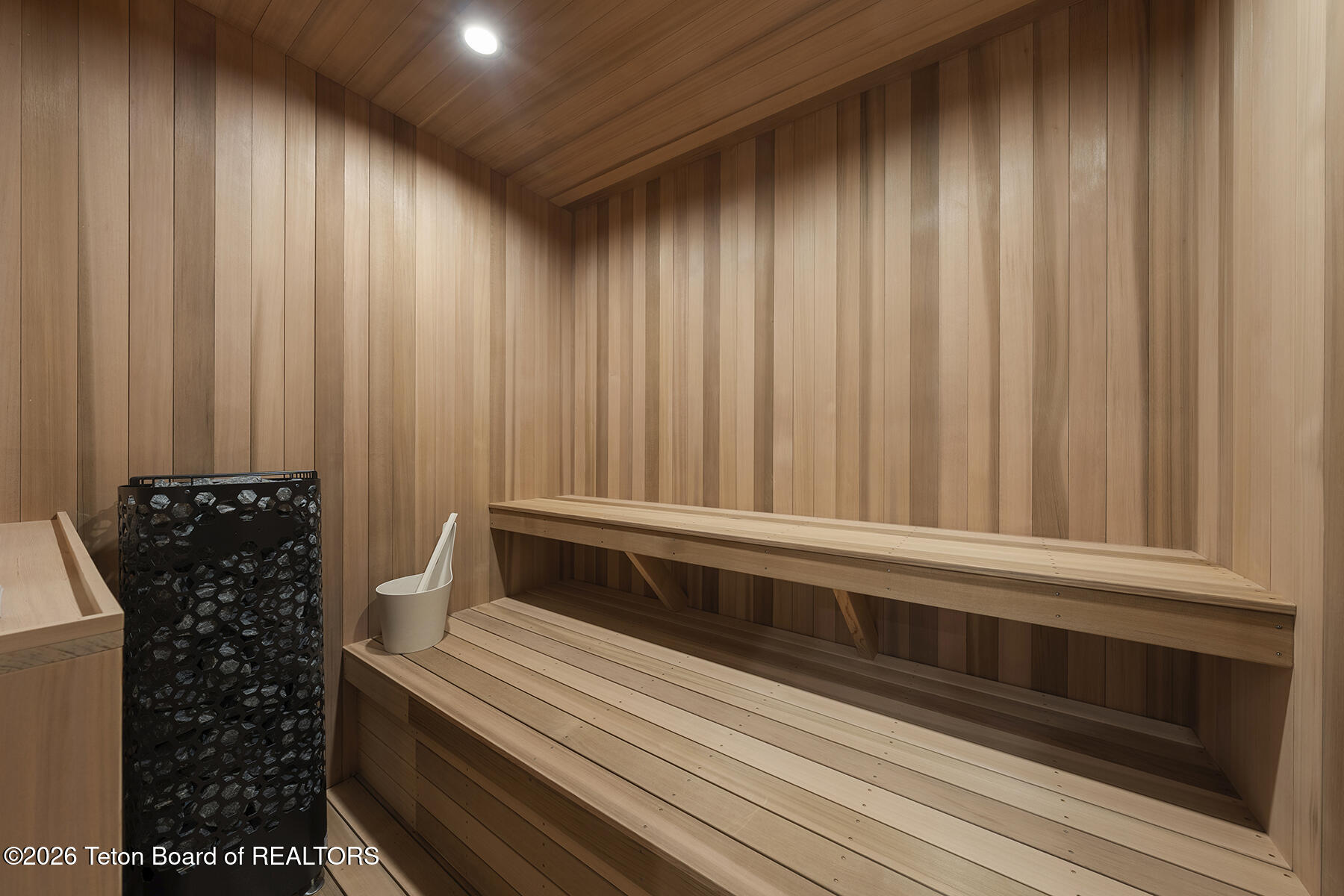 Wood-paneled sauna with tiered benches and a black stone heater.