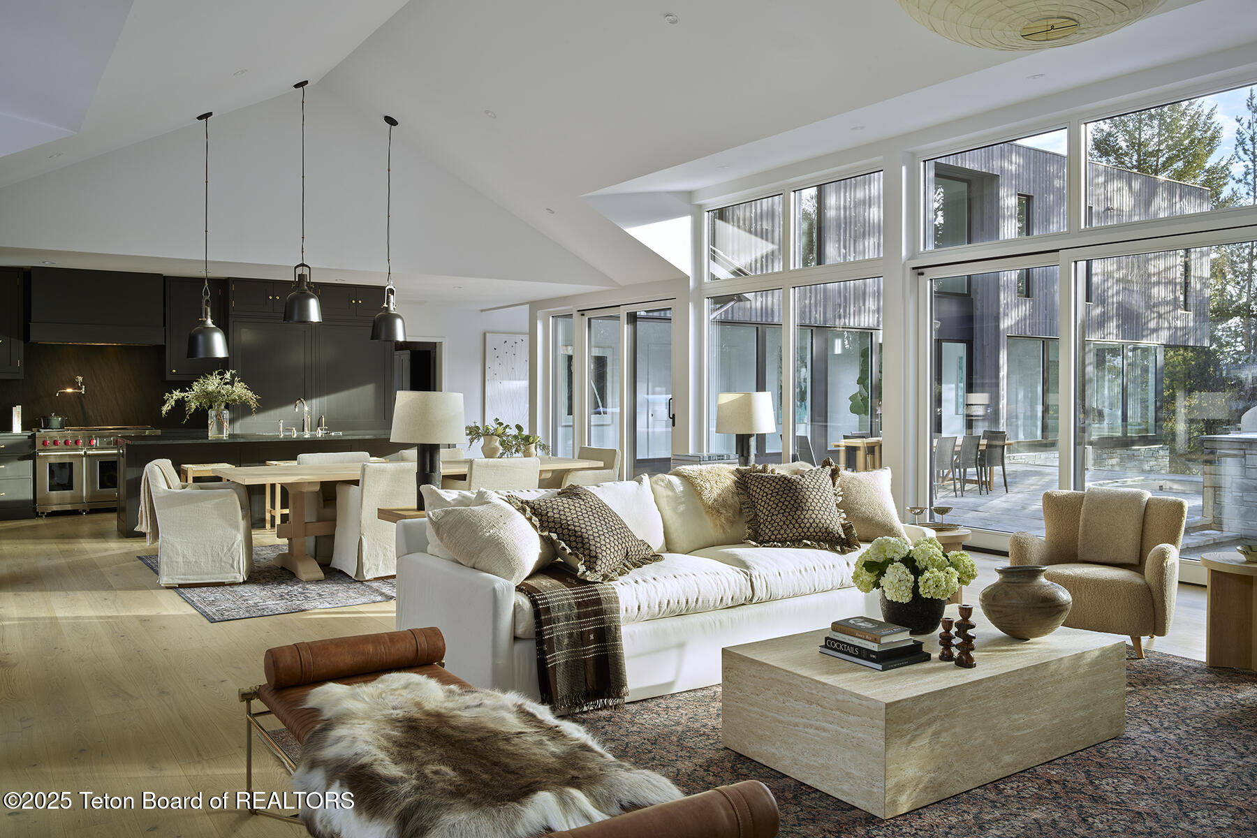 Open-plan living room with a white sofa, dark kitchen cabinetry, and expansive windows.