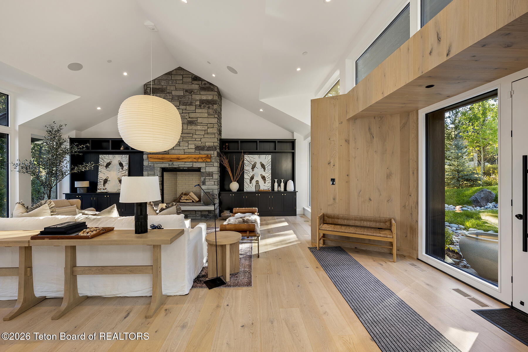 Living room with a vaulted ceiling, stone fireplace, dark built-ins, and garden-facing glass doors.
