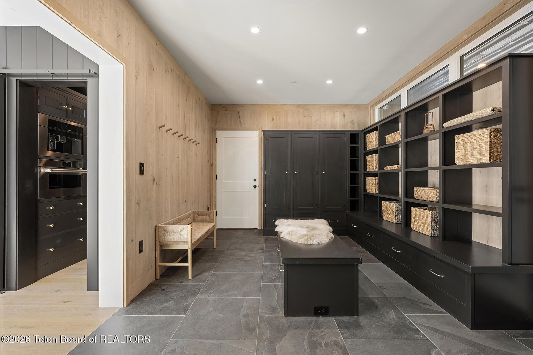 Mudroom with dark built-in storage, woven baskets, a central island, and pale wood-paneled walls.