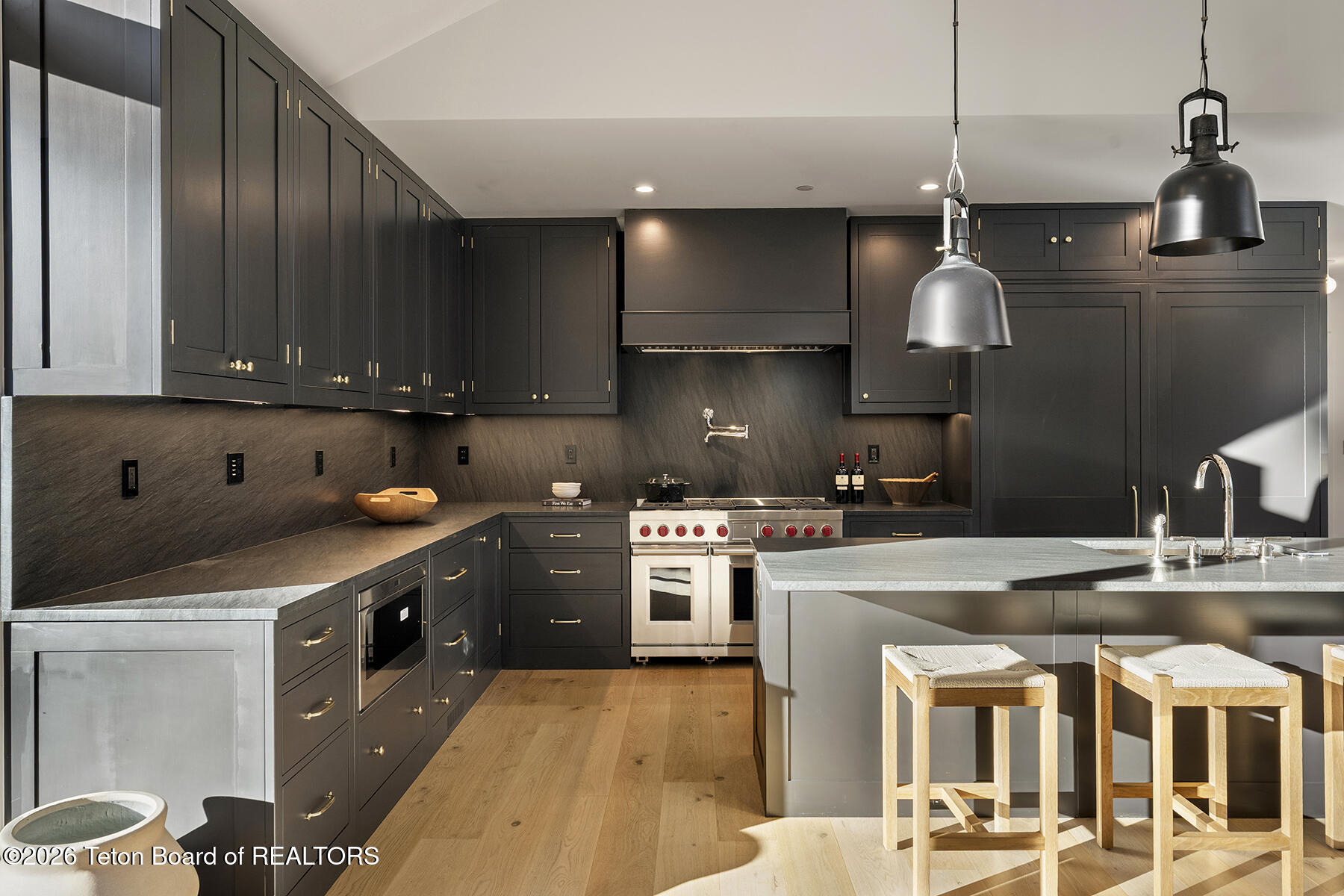 Modern kitchen with dark cabinetry, brass hardware, a stainless range, and a large island with wooden stools.