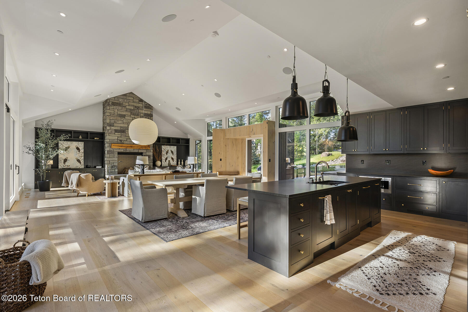 Open-plan kitchen and living room with dark cabinetry, a large island, and a stone fireplace.