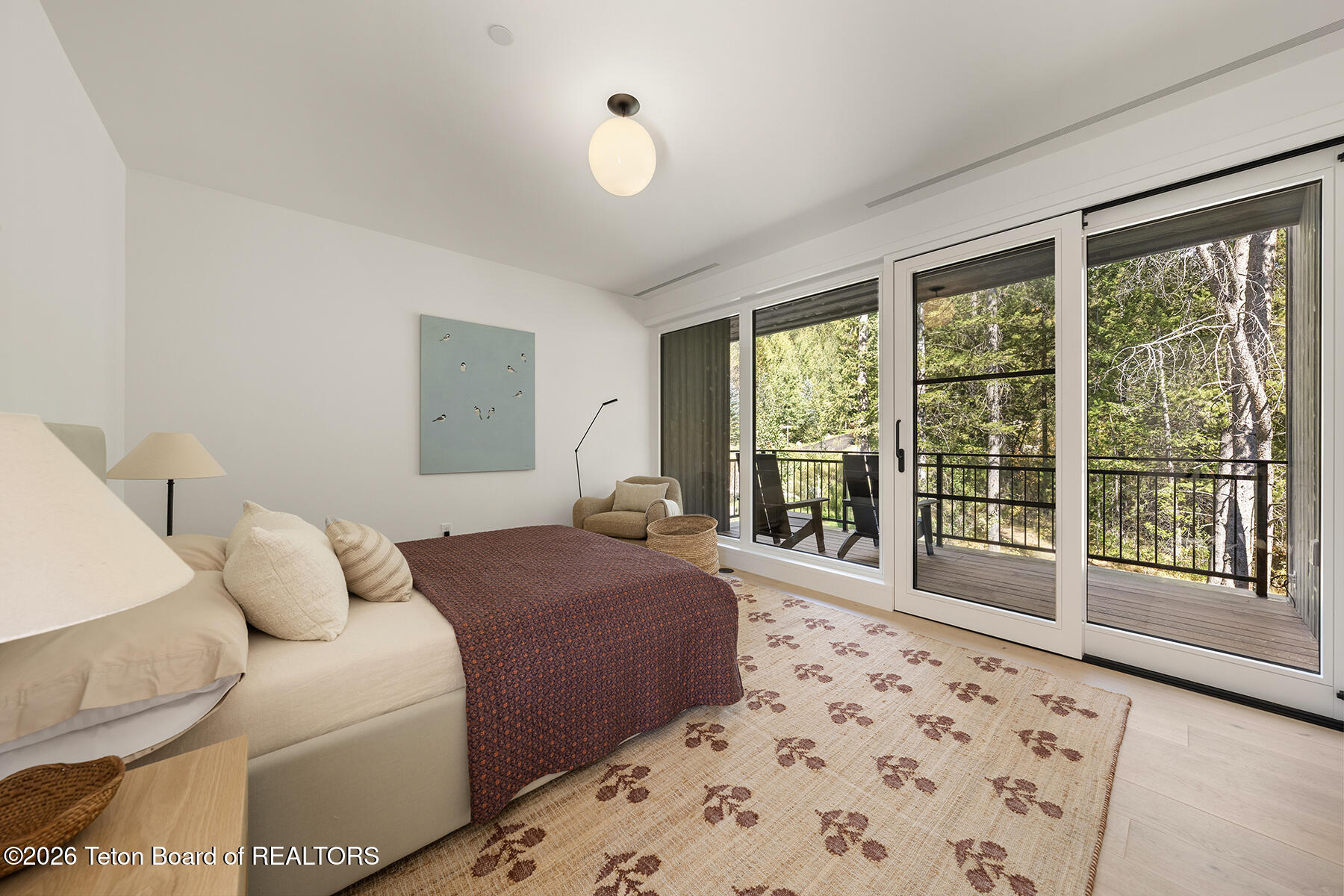 Furnished bedroom with sliding glass doors to a balcony overlooking trees.