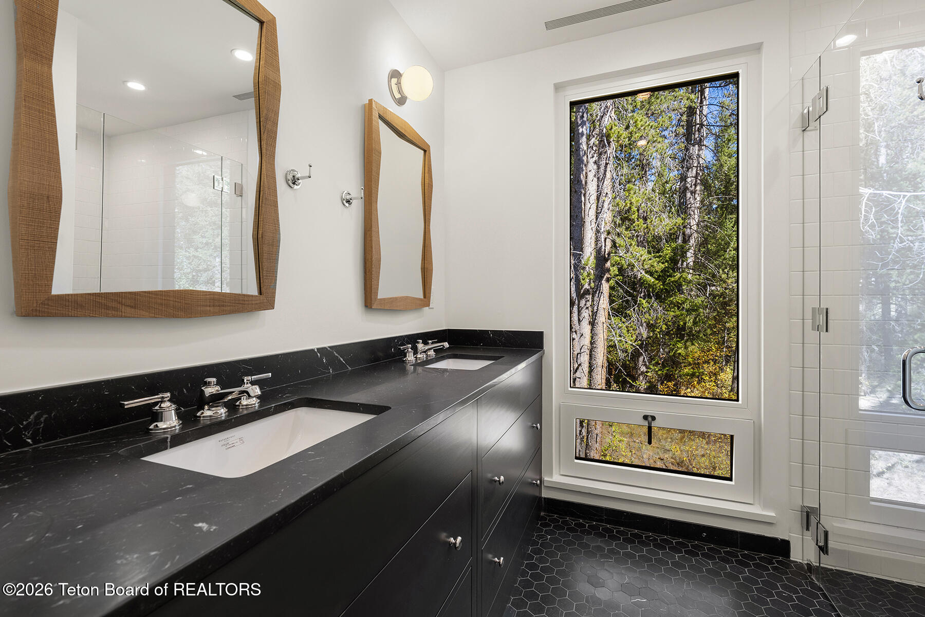 Bathroom with a black double-sink vanity and a large window overlooking autumn trees.