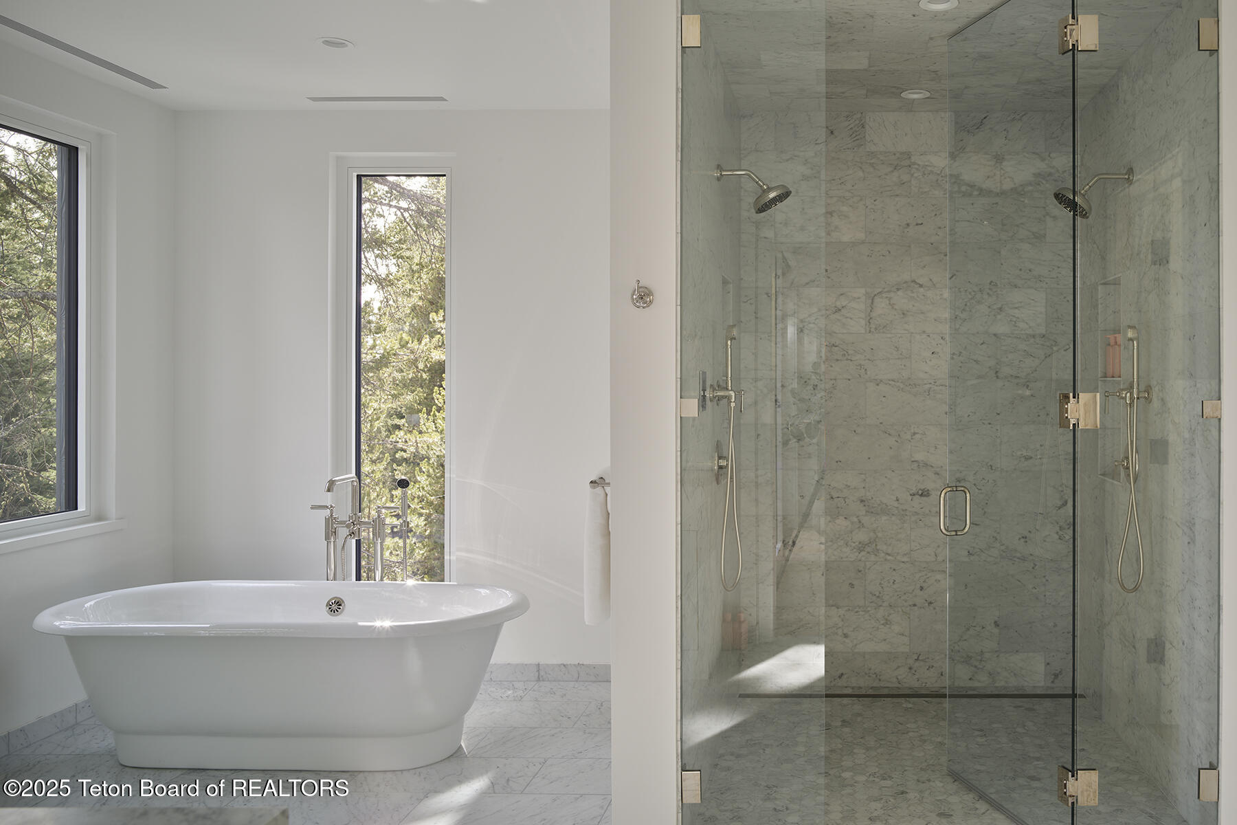 Bathroom with a freestanding tub, marble shower, and tall windows overlooking trees.