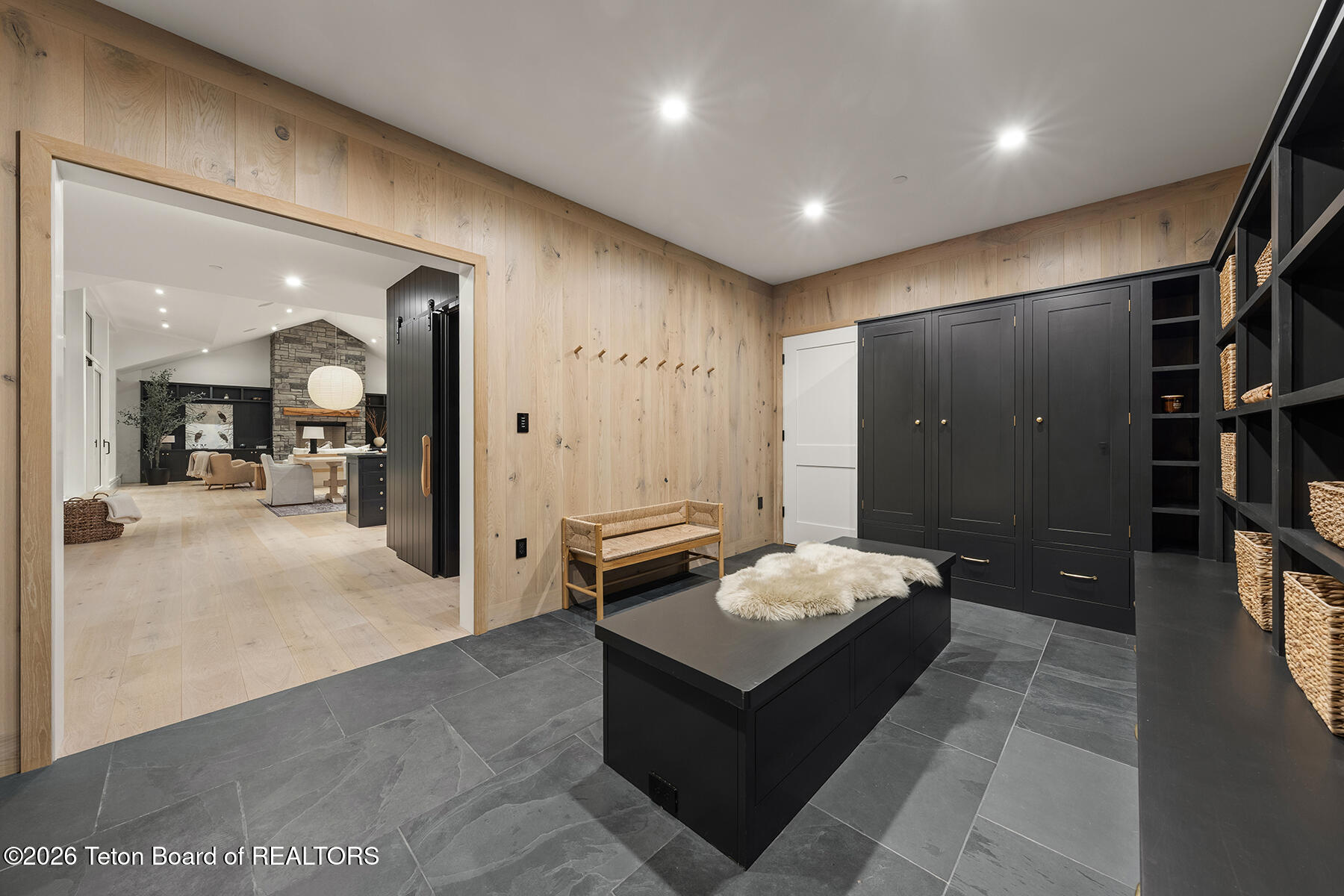 Mudroom with dark built-in storage, wall hooks, a woven bench, and a large island.