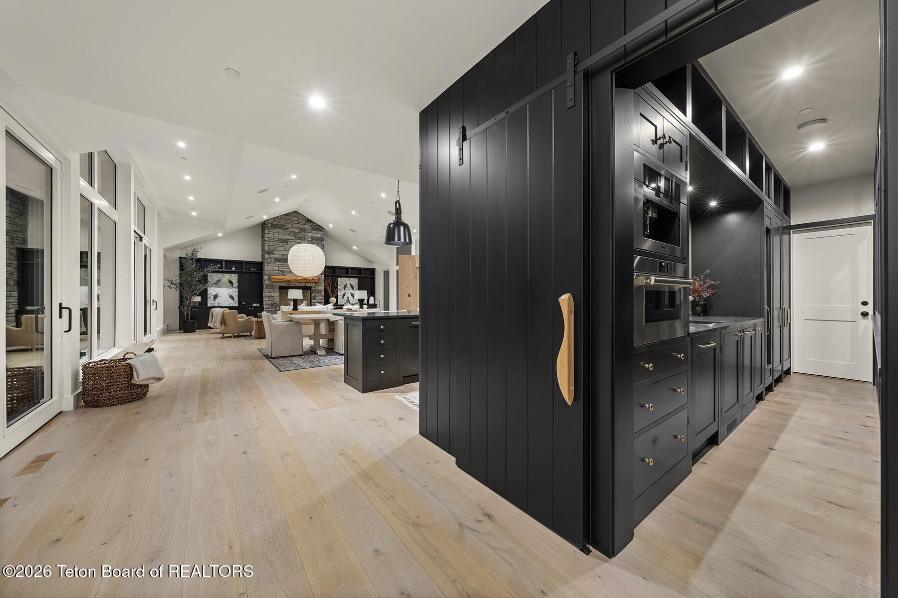 Open-plan kitchen and living area with dark cabinetry, a sliding barn door, and a stone fireplace.