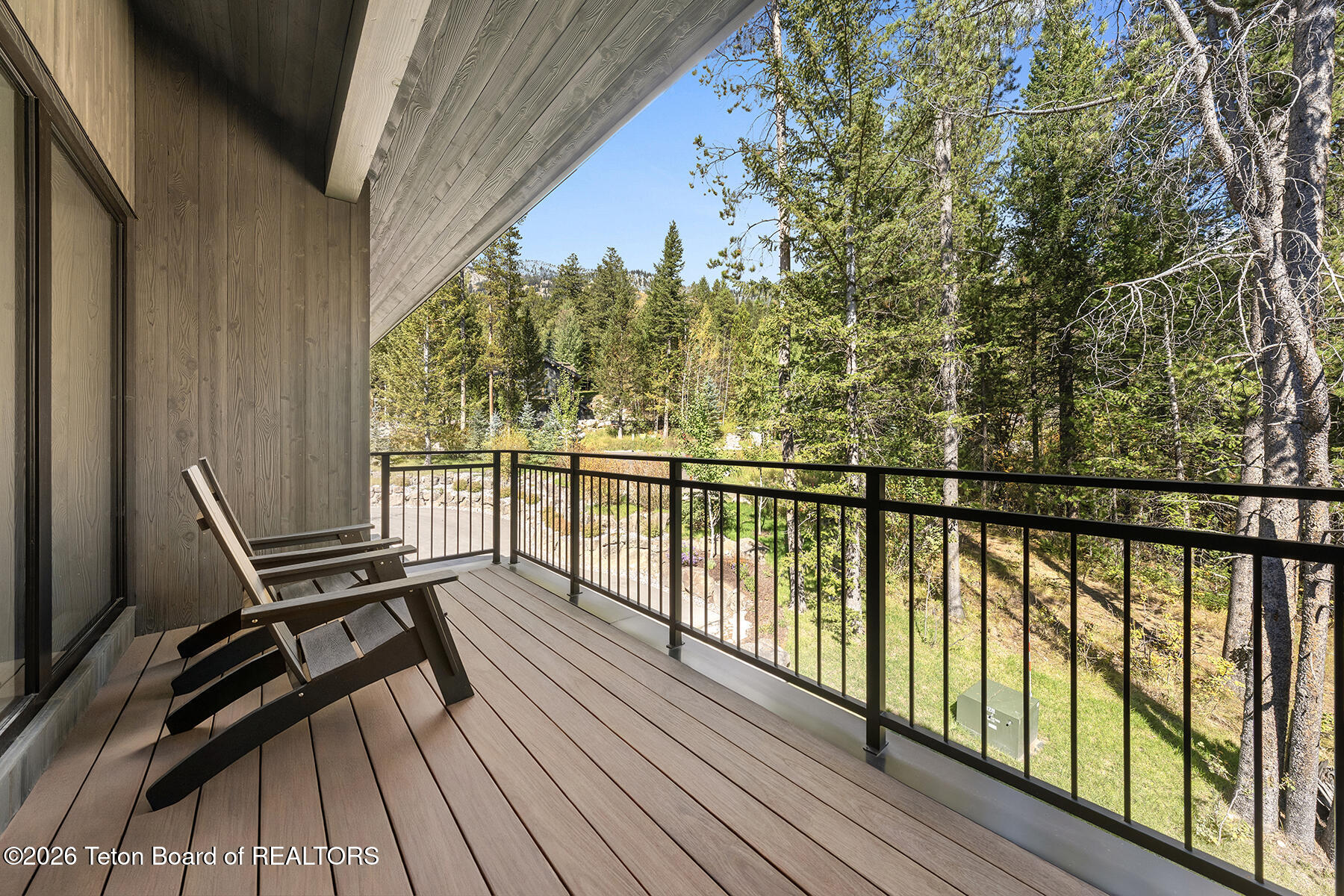 Covered wood balcony with lounge chairs overlooking a sunlit forest.