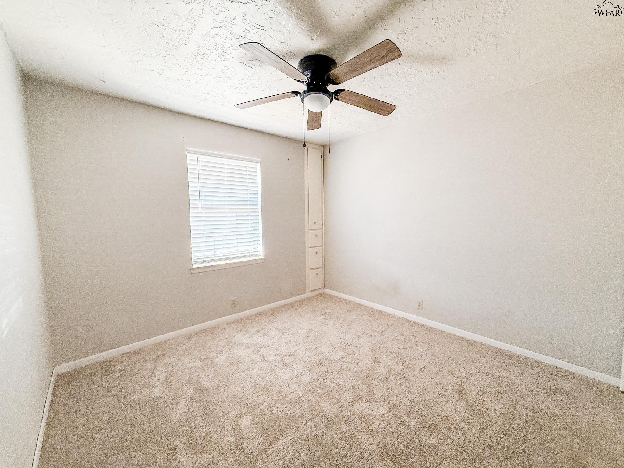 Empty carpeted bedroom with a ceiling fan, window blinds, and built-in drawers.