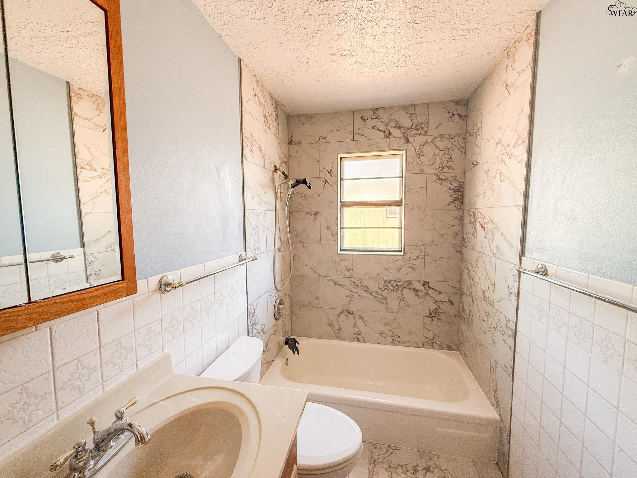 Bathroom with marble-pattern tile, a bathtub and shower, and a wood-framed mirror above the vanity.