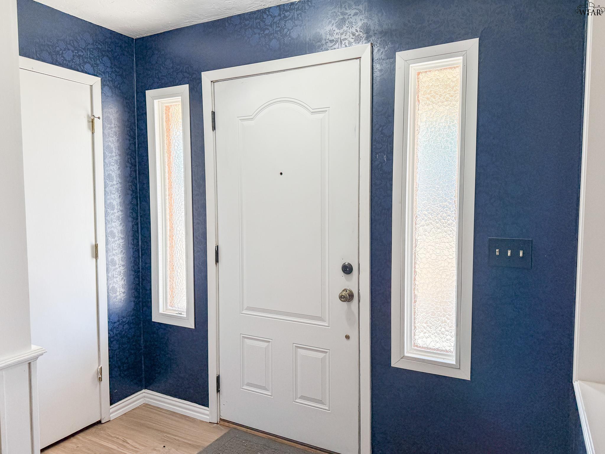 Entryway with a white front door, textured-glass sidelights, and deep blue patterned walls.